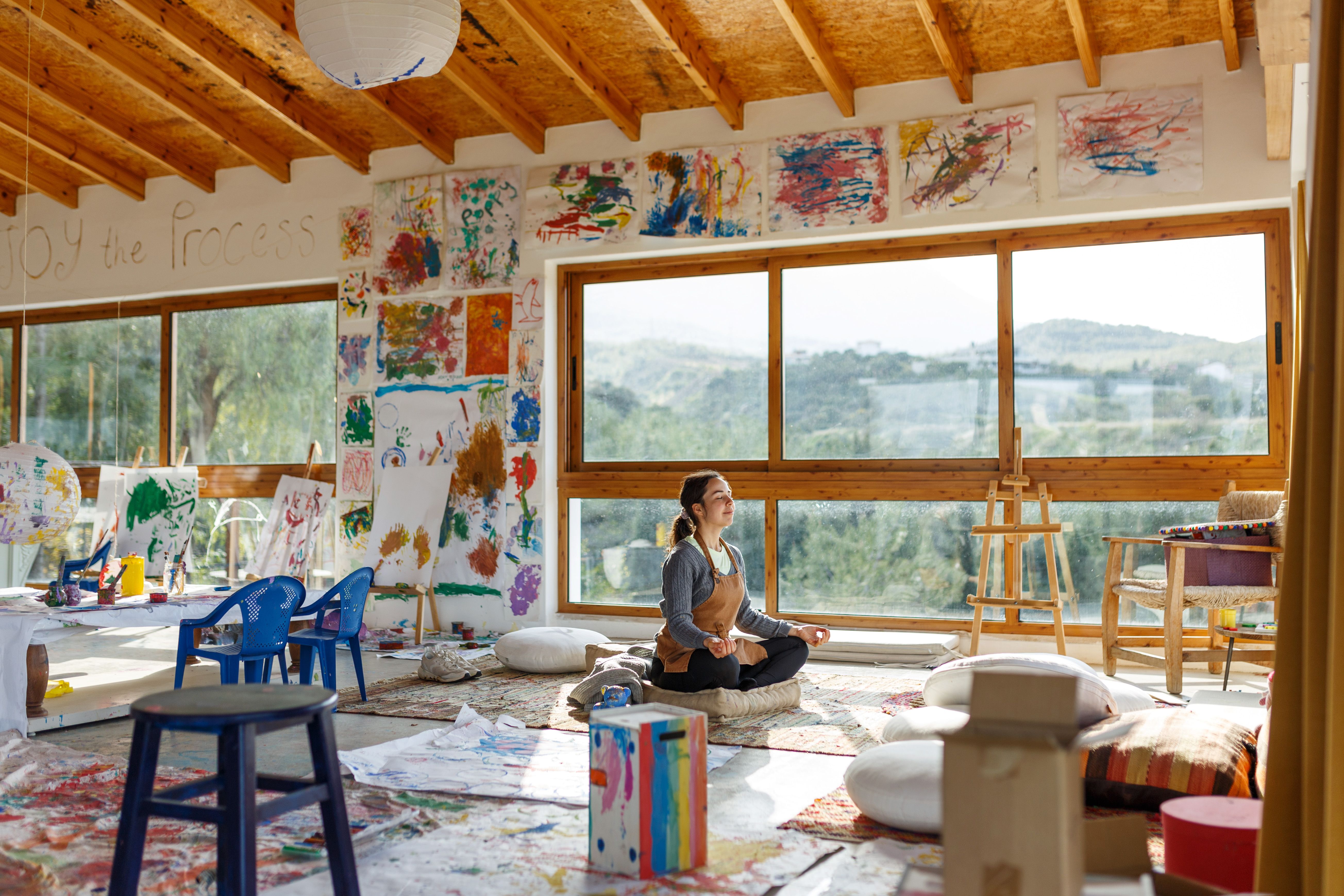 Young woman artist sitting on floor doing yoga exercise at art studio.Mindful activity and art therapy concept