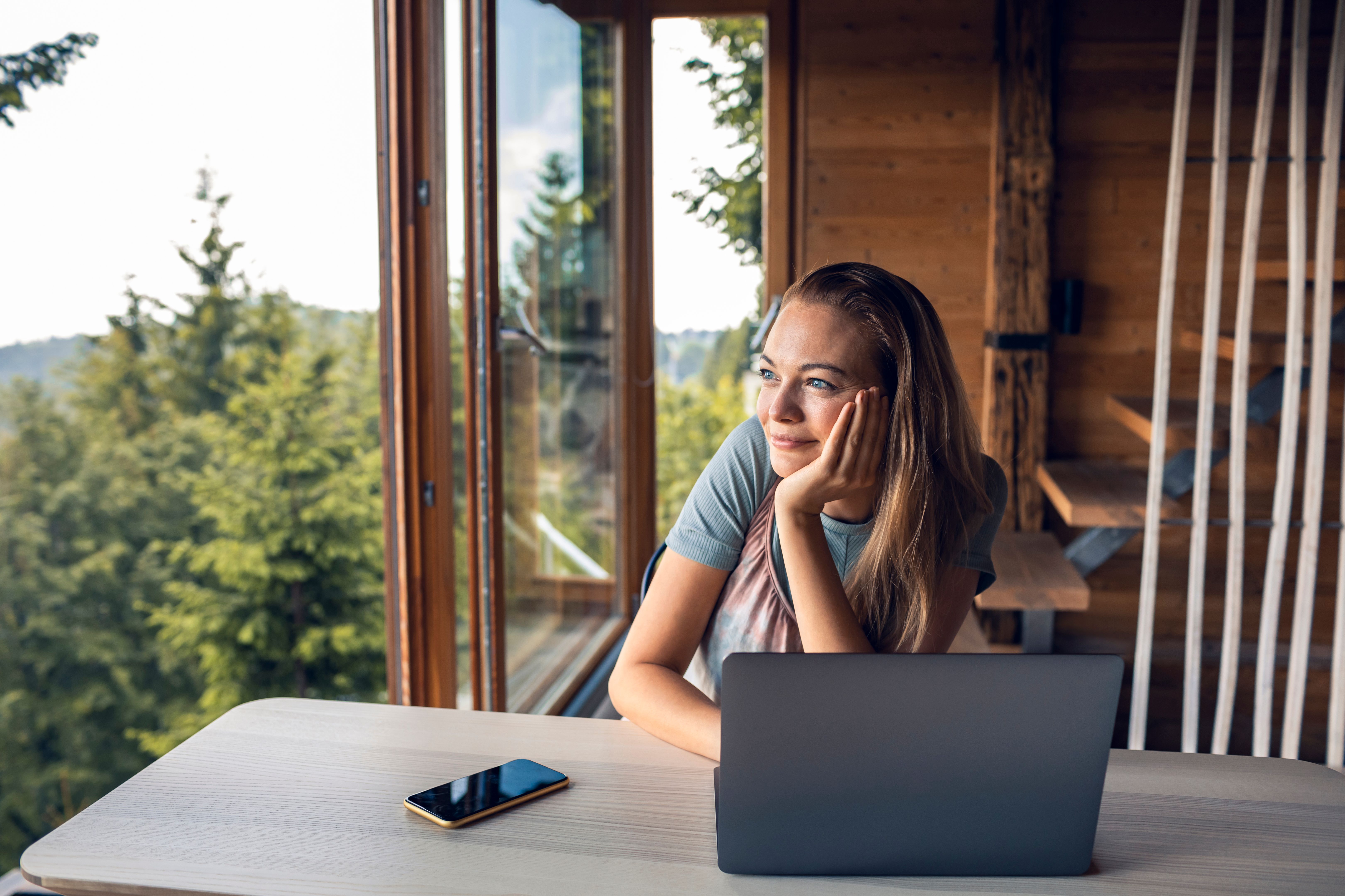 Young woman looking at the view through the window of a log cabin