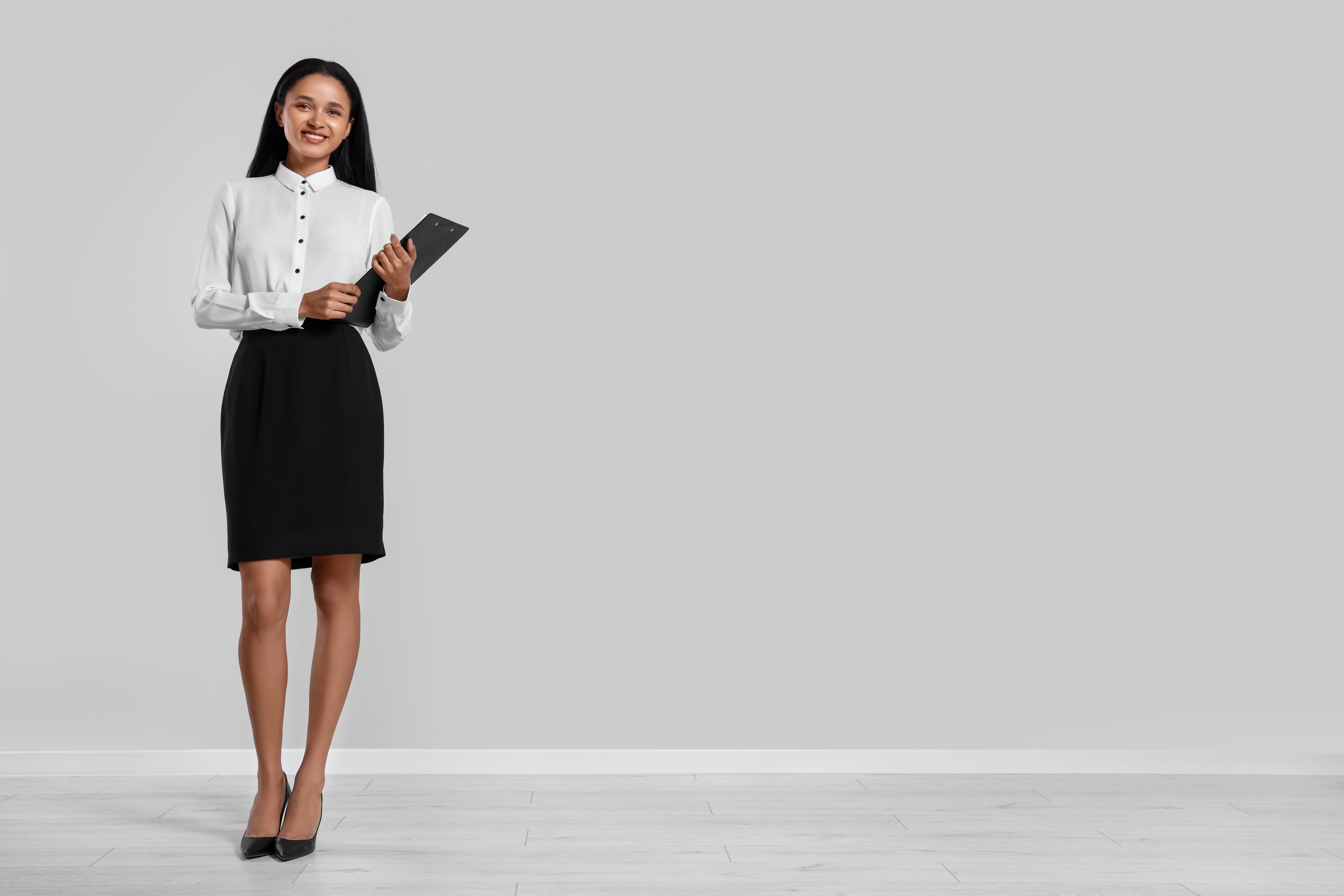 Beautiful secretary with clipboard near light gray wall in office, space for text Beautiful secretary with clipboard near light gray wall in office, space for text