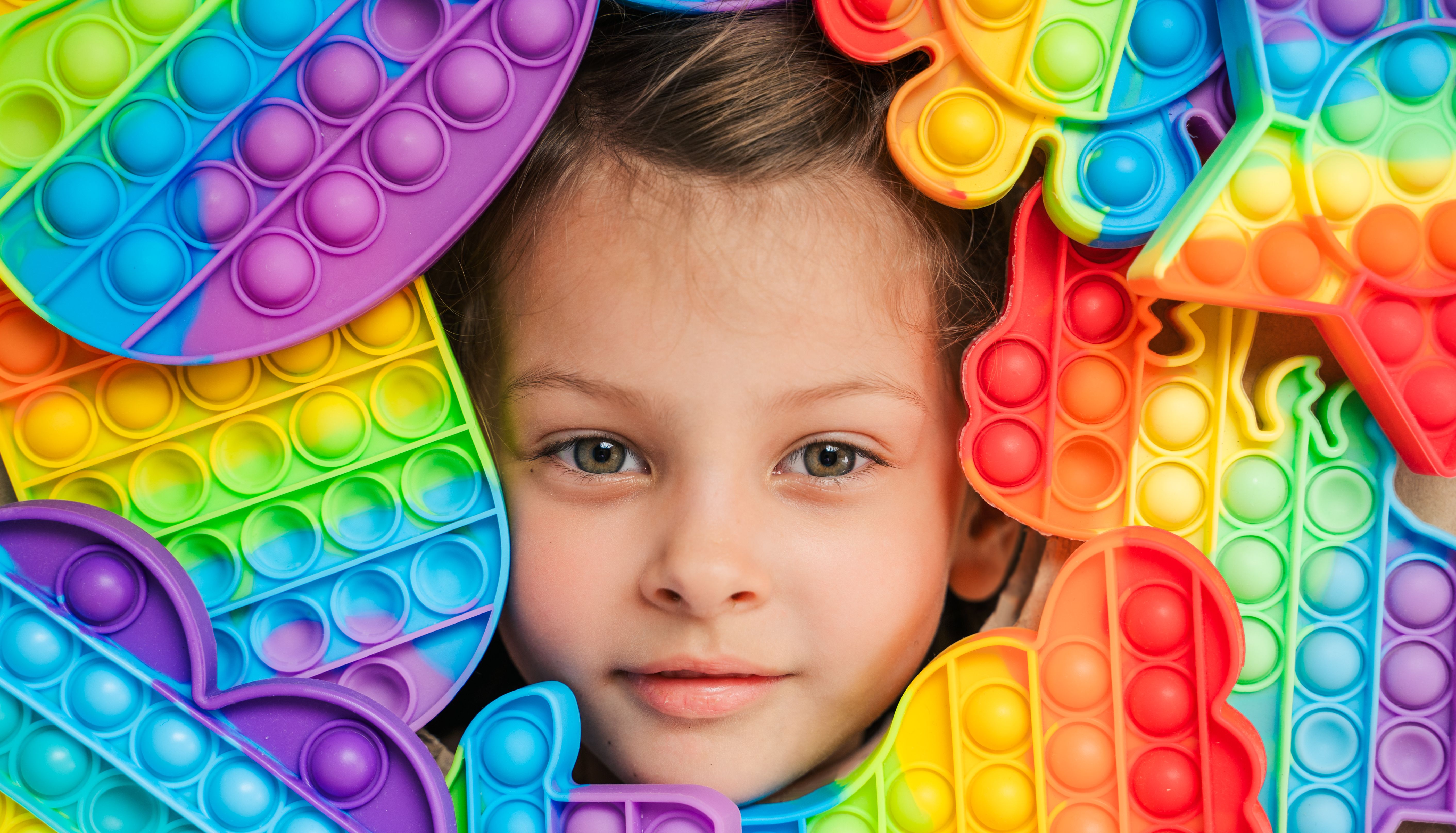 Little girl,kid,child head among many,lots of colorful pop it. Children play. Trendy silicone antistress colorful sensory push toy popit. Flapping fidget. Rainbow color.Cure of autism.Stress reliever