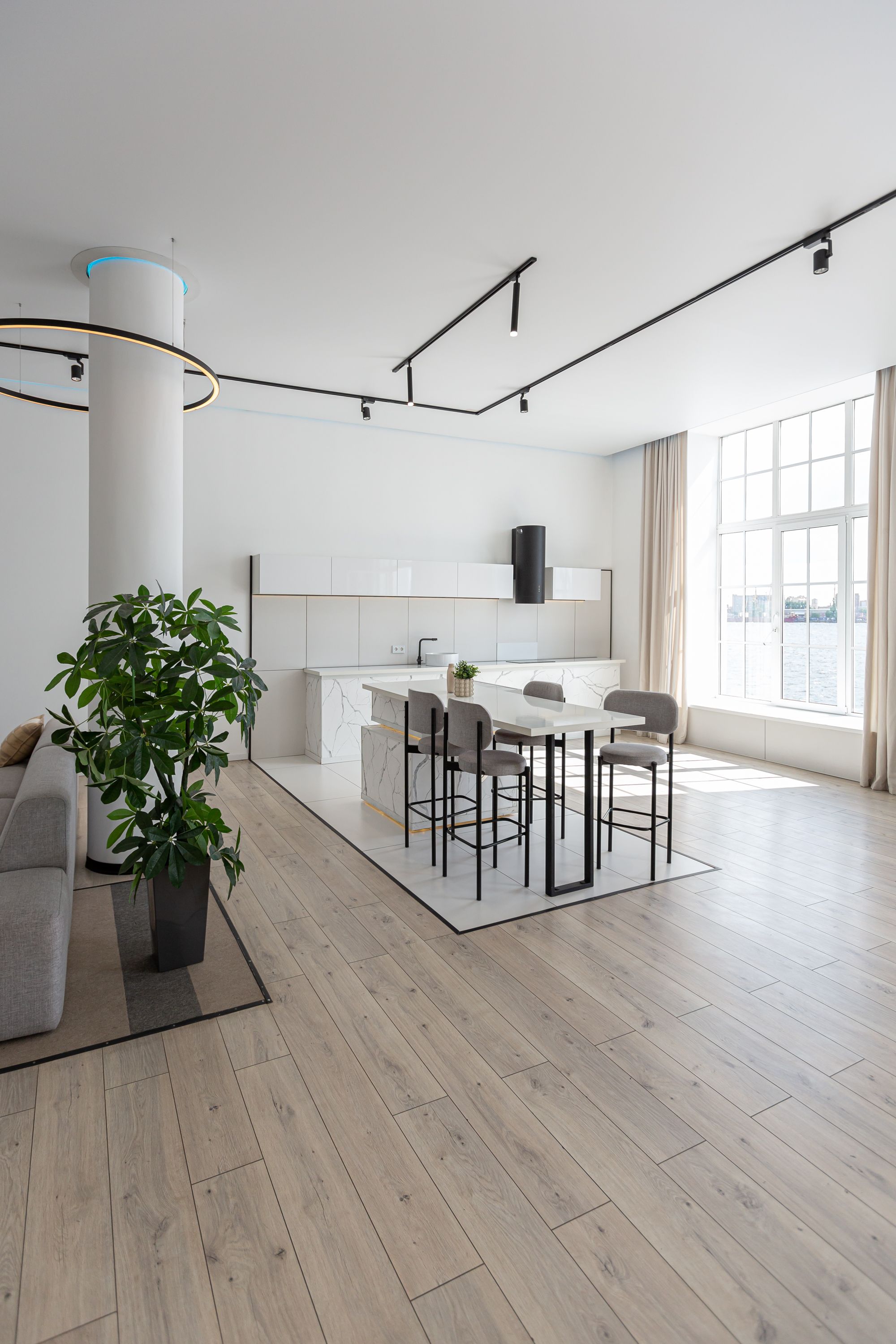 kitchen and dining island with high bar stools in a minimalistic modern luxury design of an expensive house on a sunny day. white walls with plaster, parquet, decorative lighting and no one inside