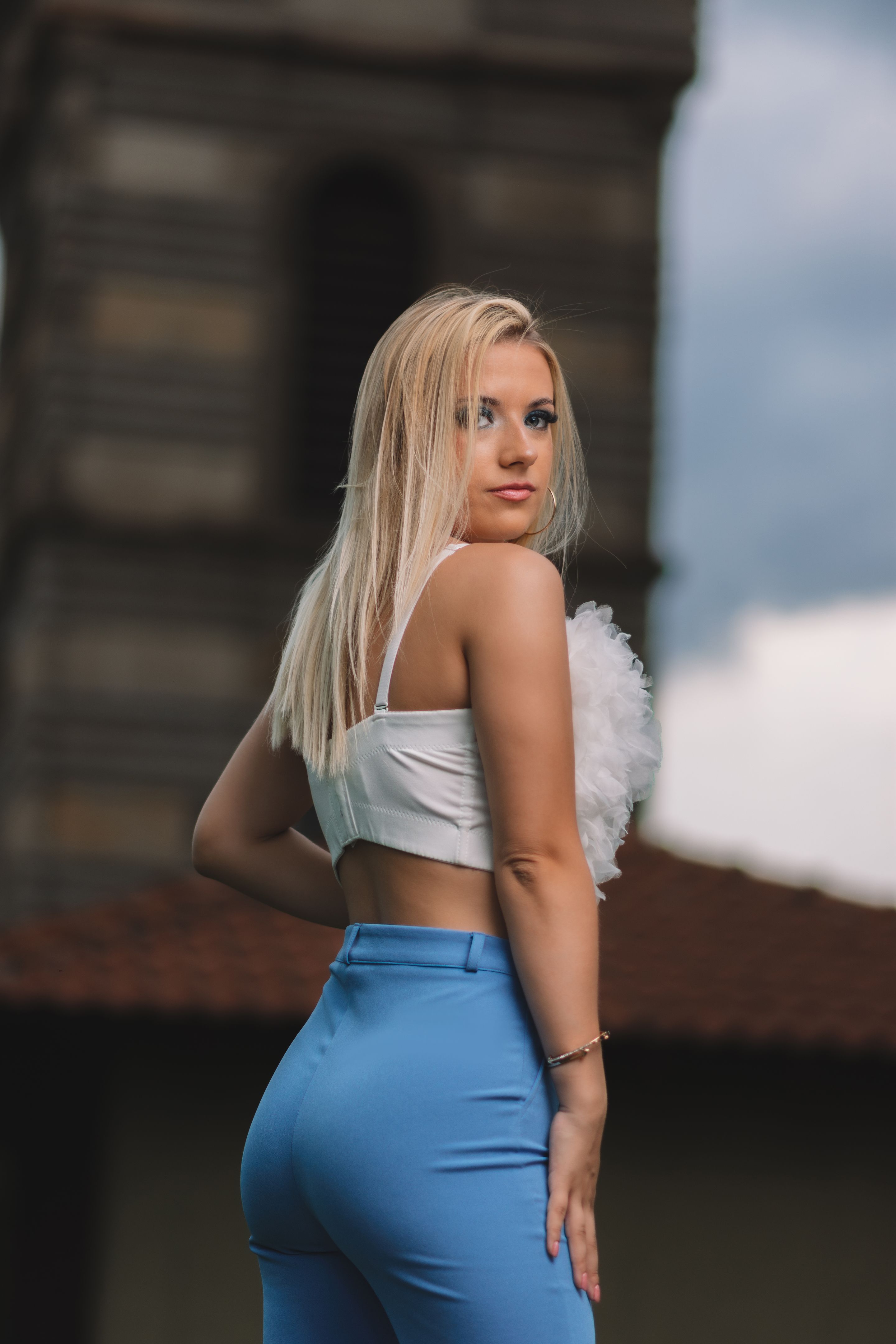 Beautiful confident young woman with her back turned and looking over her shoulder posing in blue pants