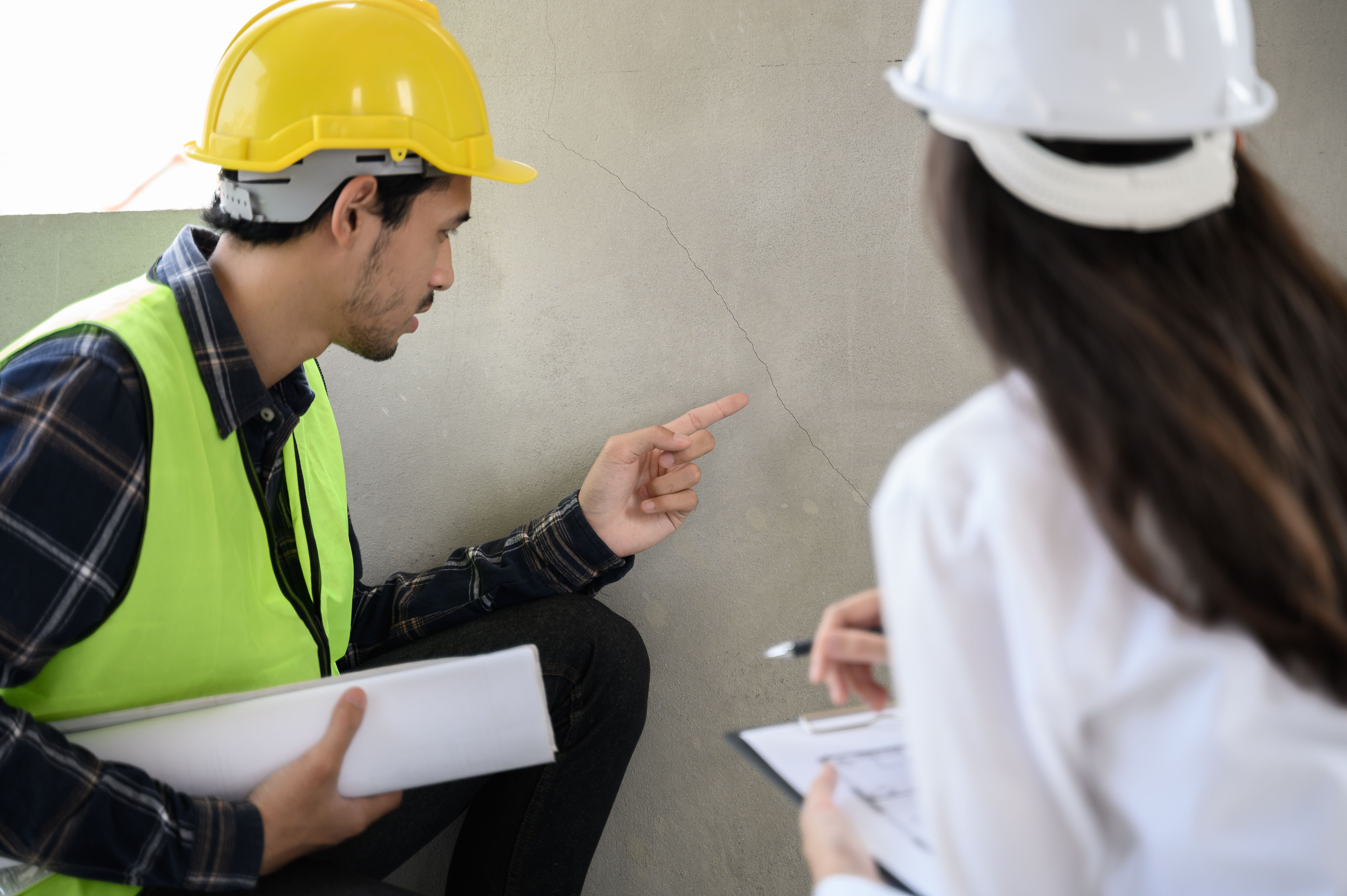 Male civil engineer with inspection check sheet consult with construction site foreman technician for inspect building condition defect pointing wall crack wait for repair.