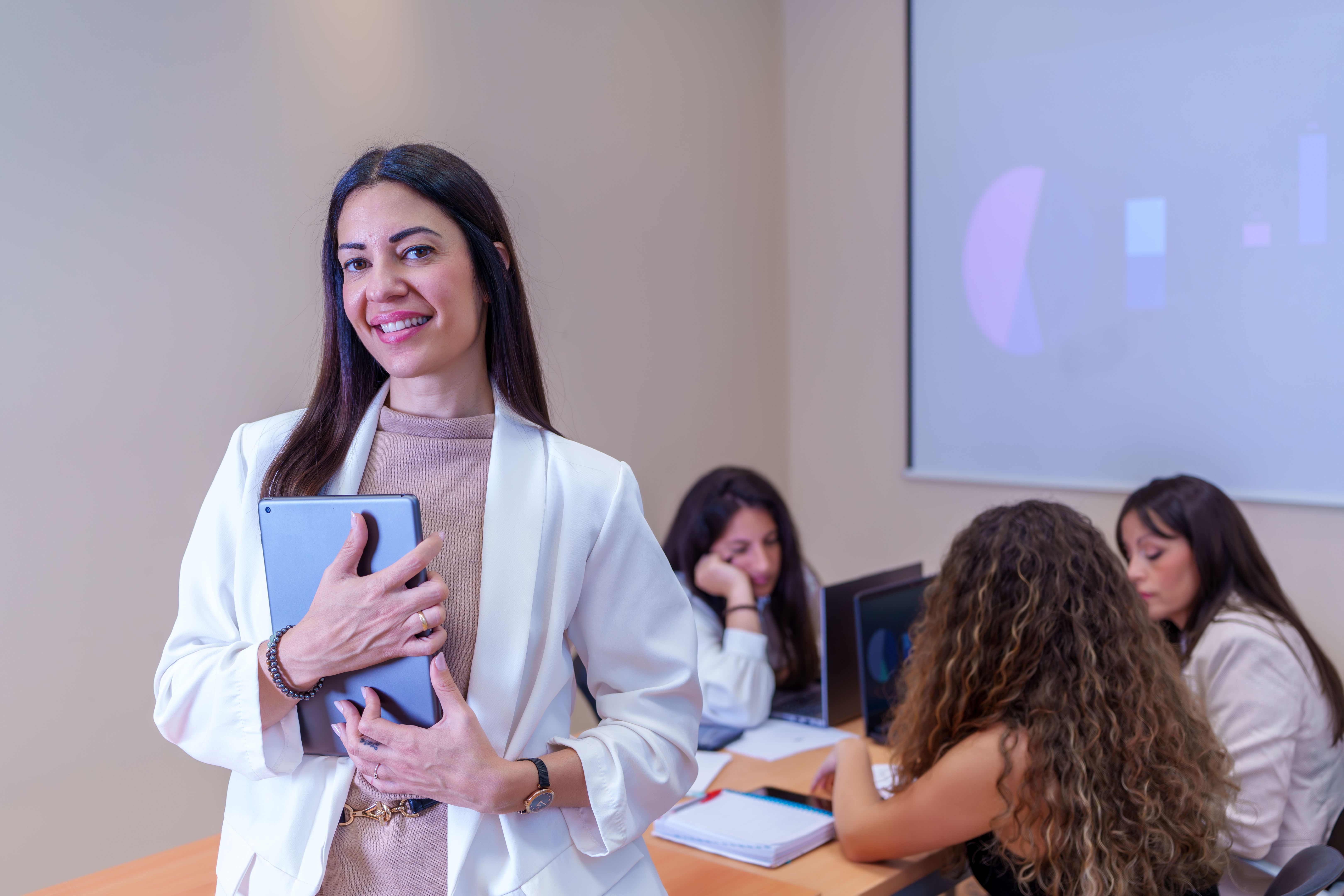 Smiling teacher holding tablet with students working in background in classroom