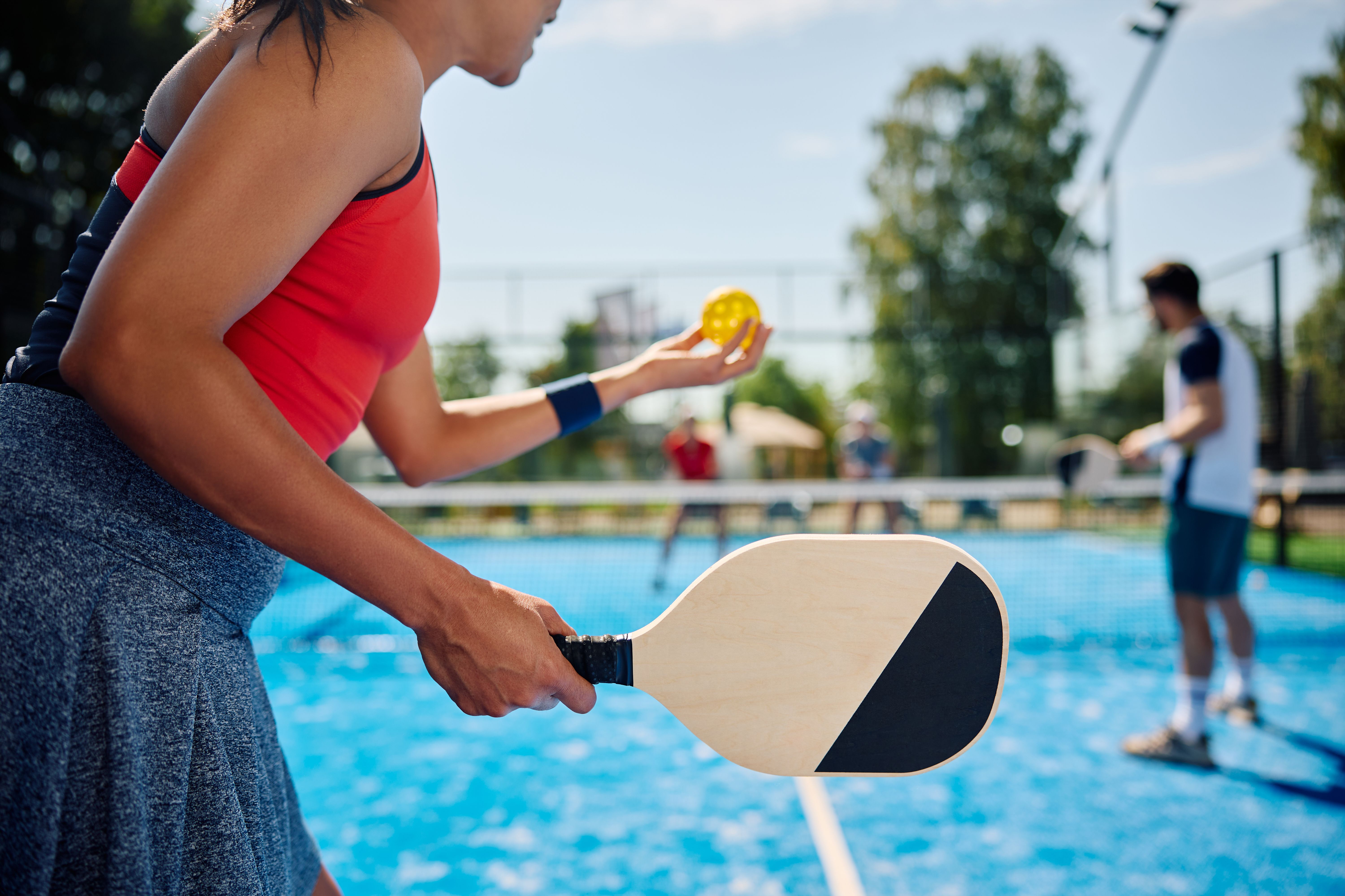 Black female pickleball player serving the ball during the match on outdoor court.