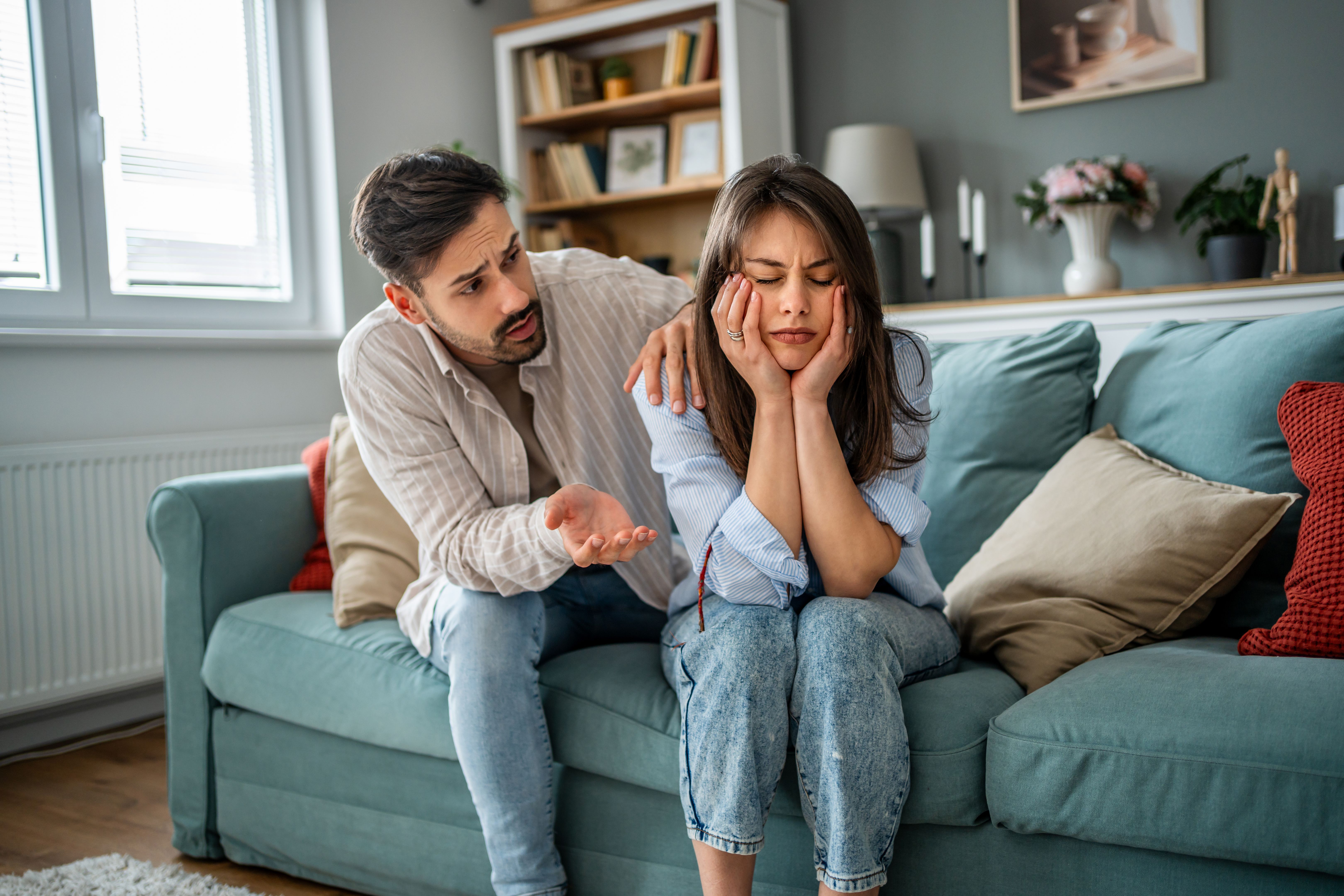 Young man comforting sad girlfriend at home on sofa