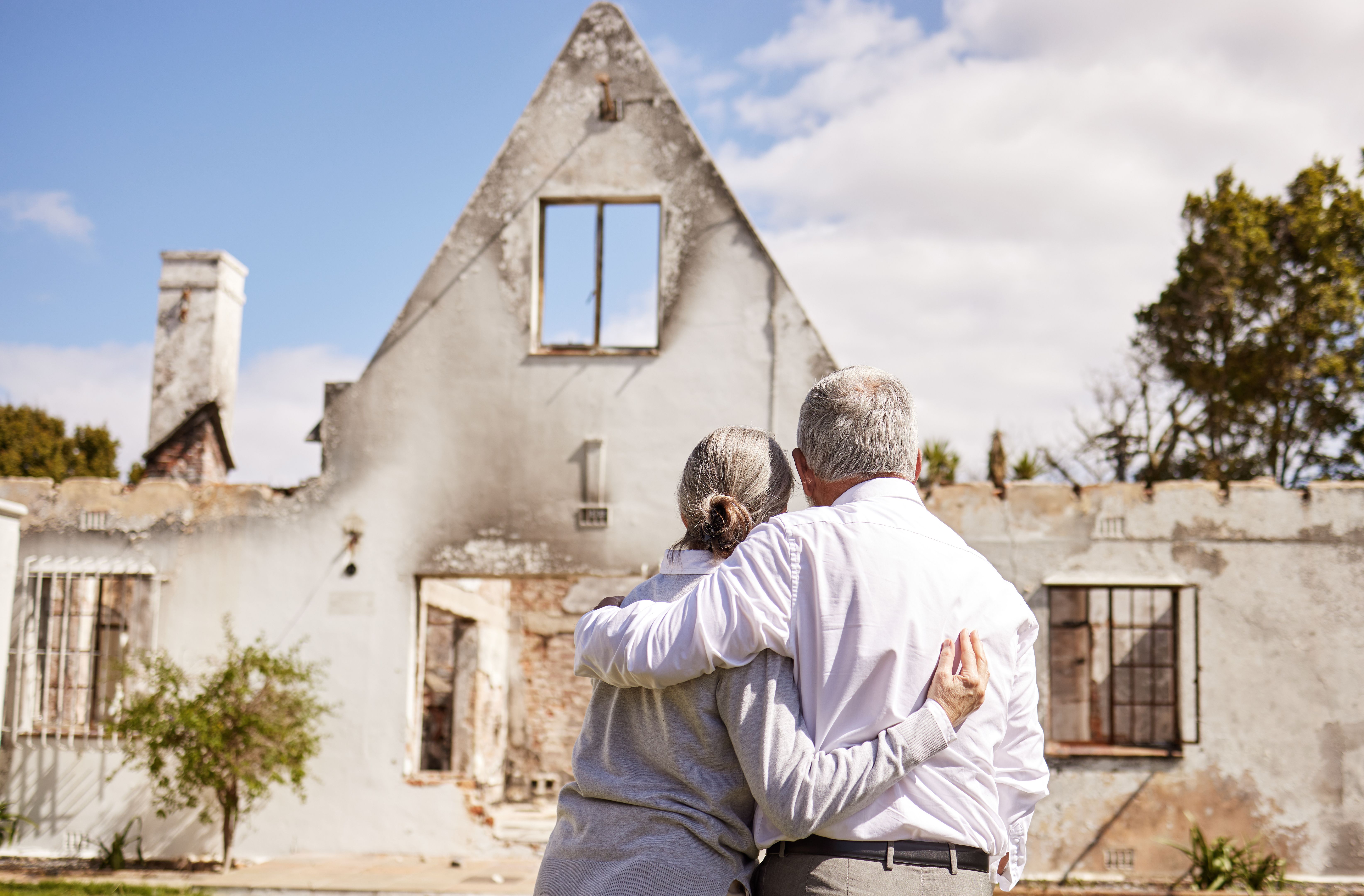 Photo d’un couple de personnes âgées se réconfortant mutuellement après avoir perdu leur maison dans un incendie