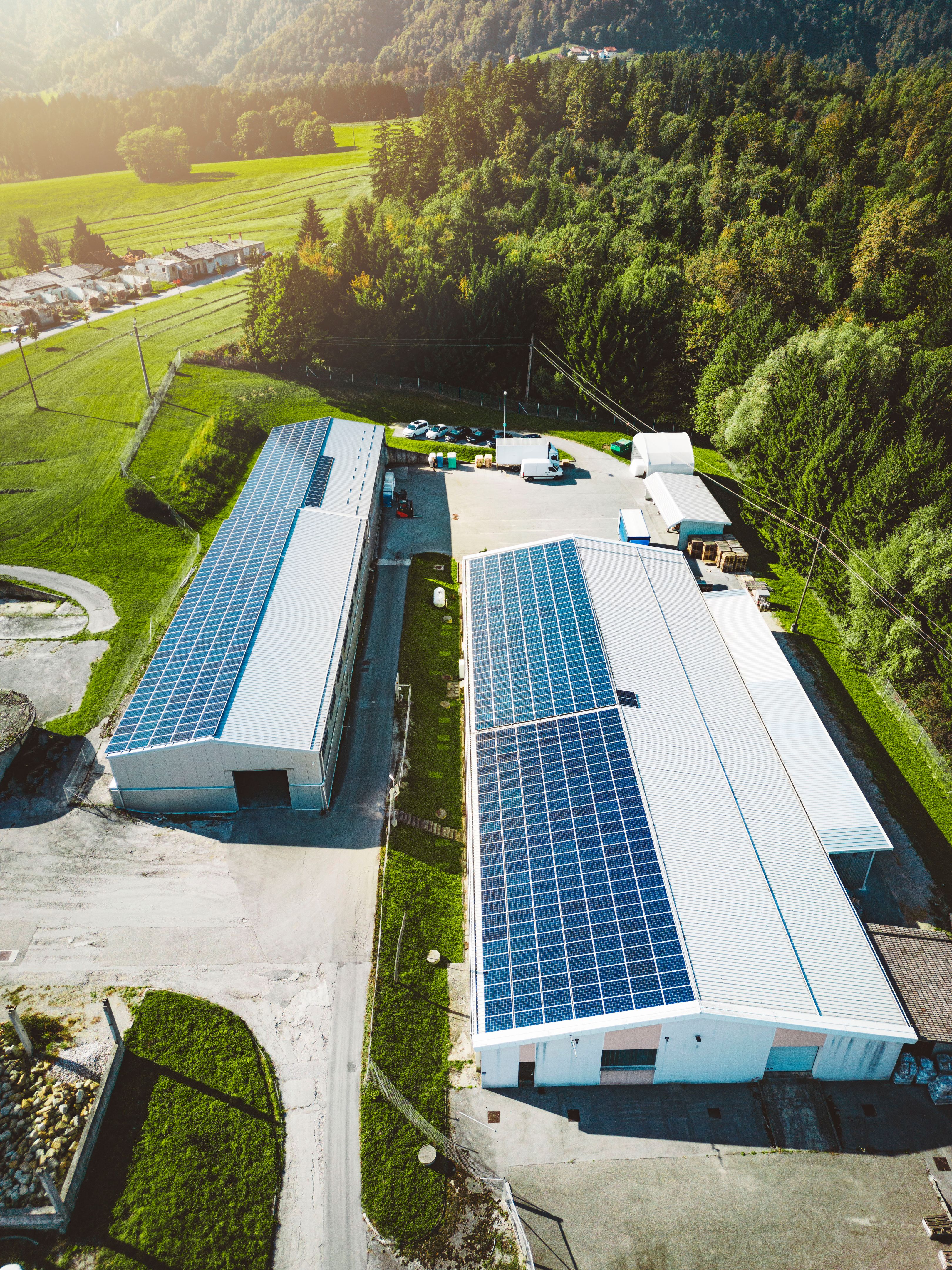 Vertical photo of two industrial buildings with a roof covered in solar panels - renewable energy