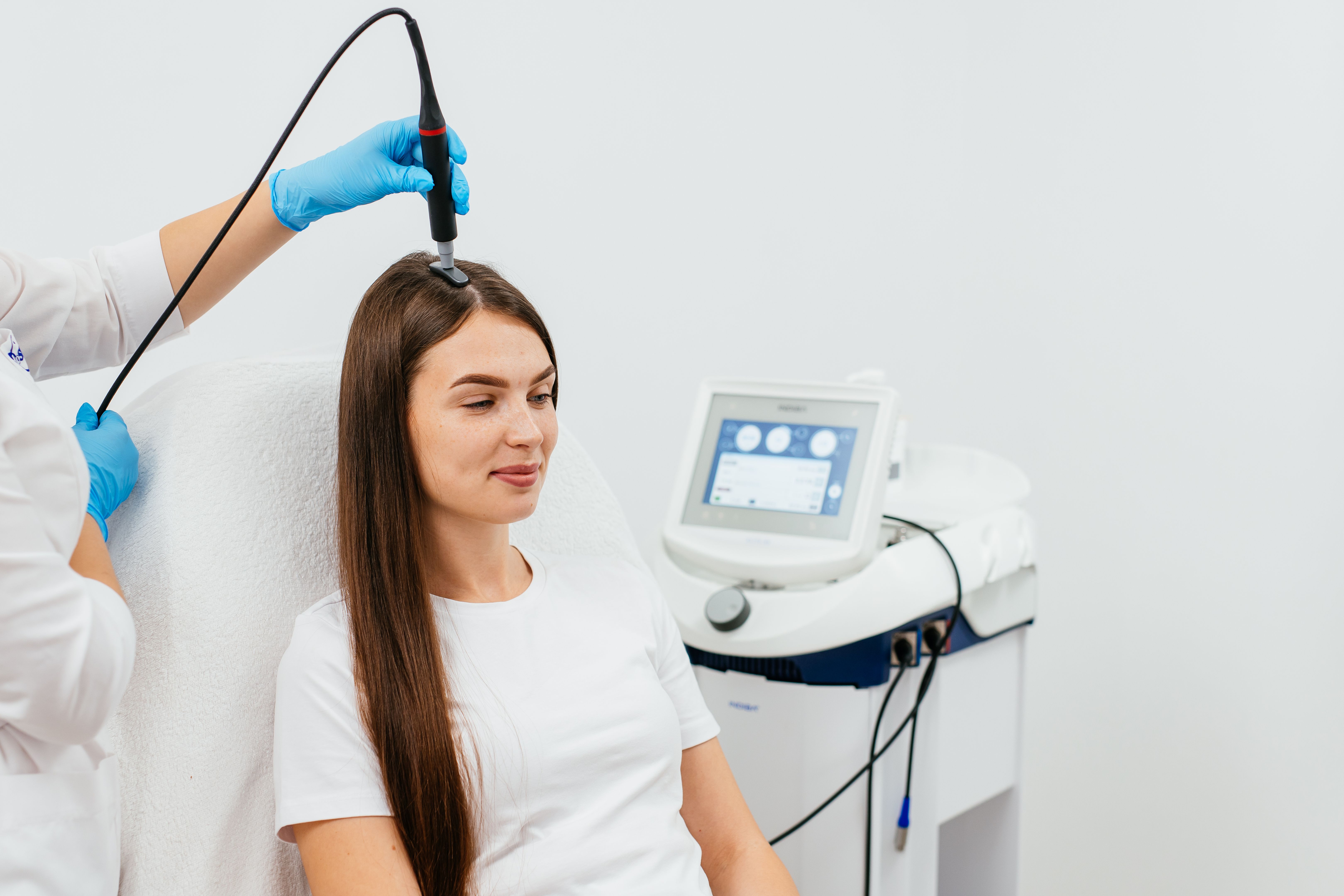 A young beautiful woman is doing a procedure to improve hair and scalp growth. Doctor's hands in blue gloves. Hair treatment in cosmetology using new technologies.