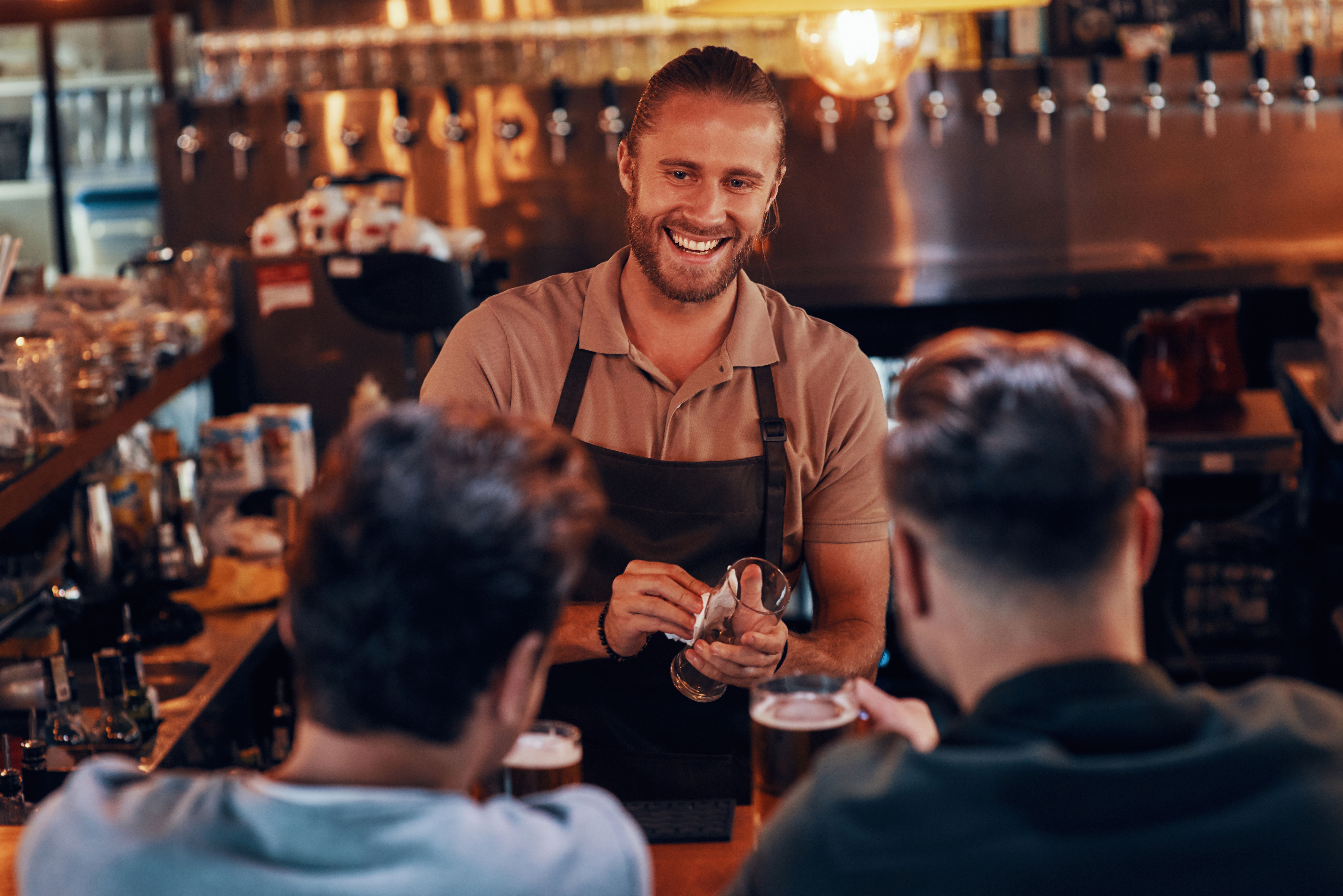 Young bartender serving beer to young men