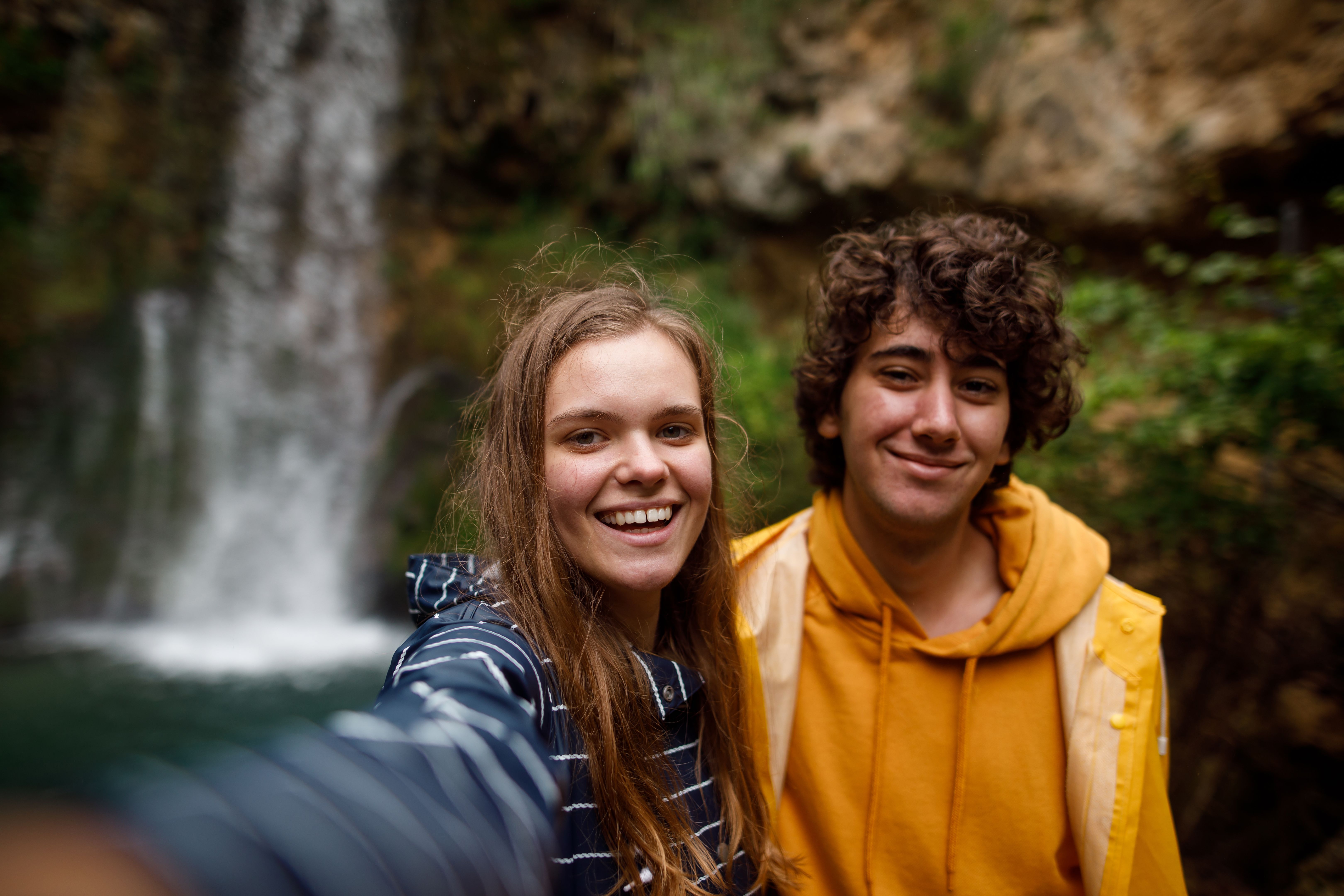 Young couple taking selfie in front of mountain waterfall
