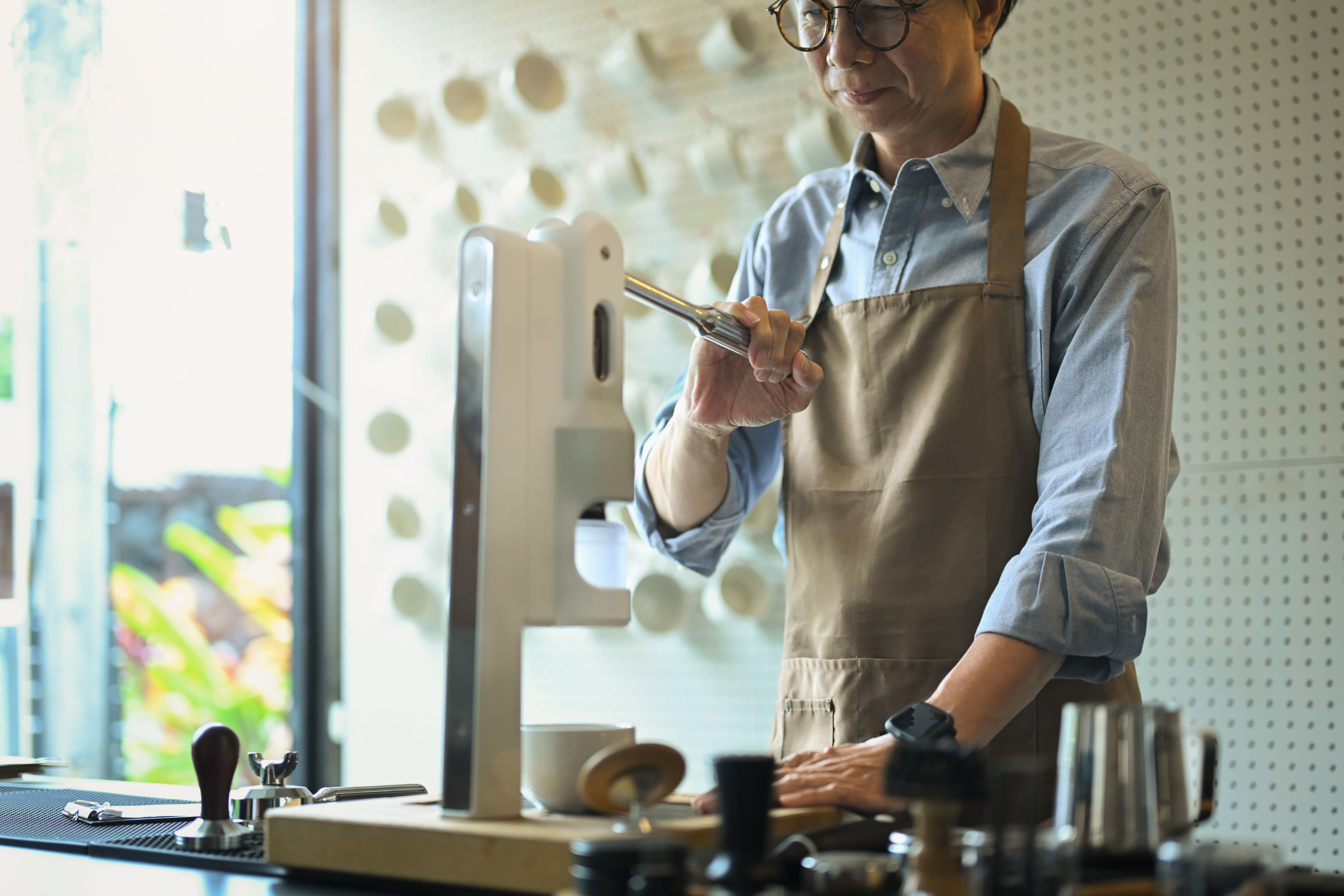 Smiling wearing apron preparing coffee for customers at his cafe counter