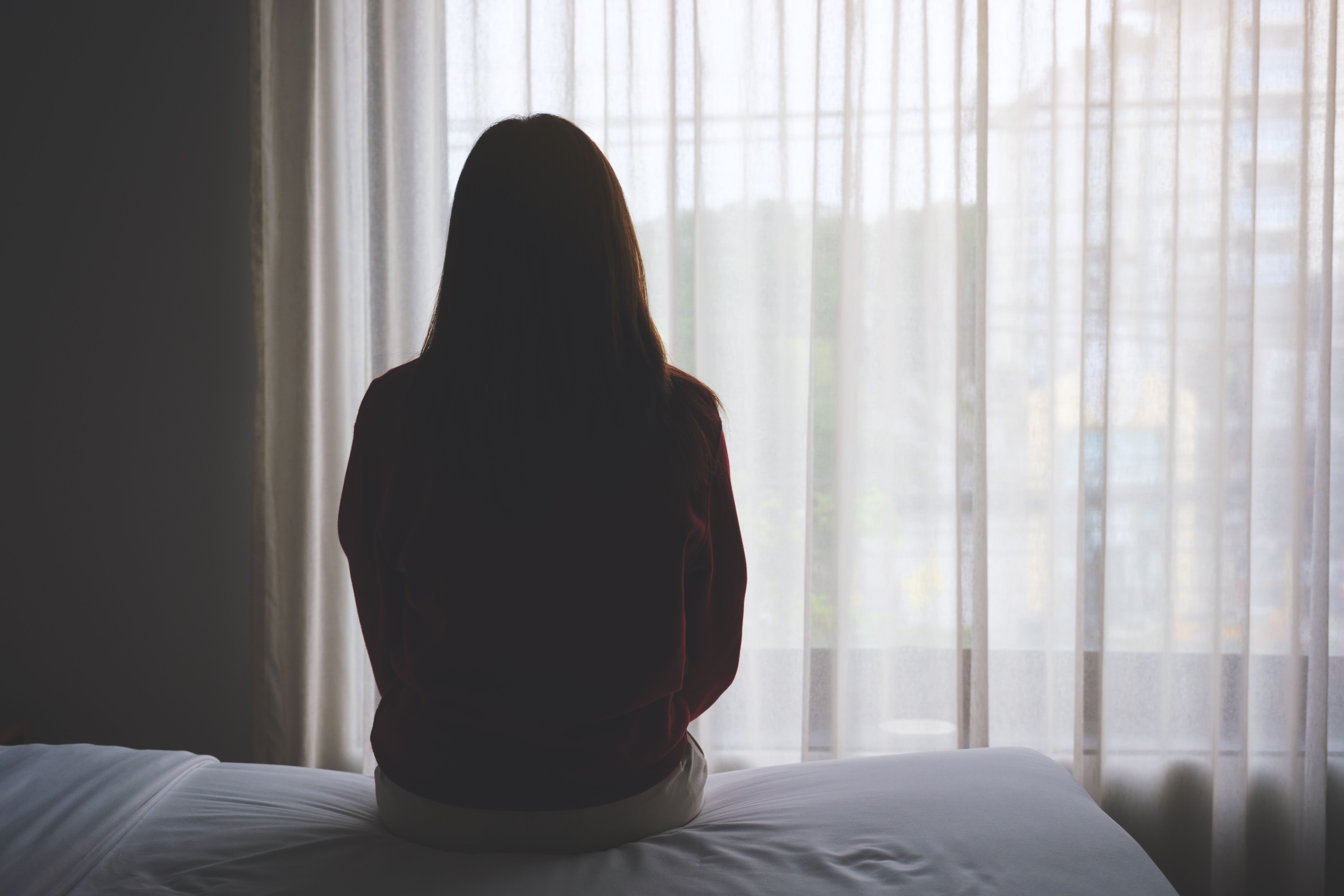 Rear view image of a woman sitting alone on a bed in bedroom Rear view image of a woman sitting alone on a bed in bedroom