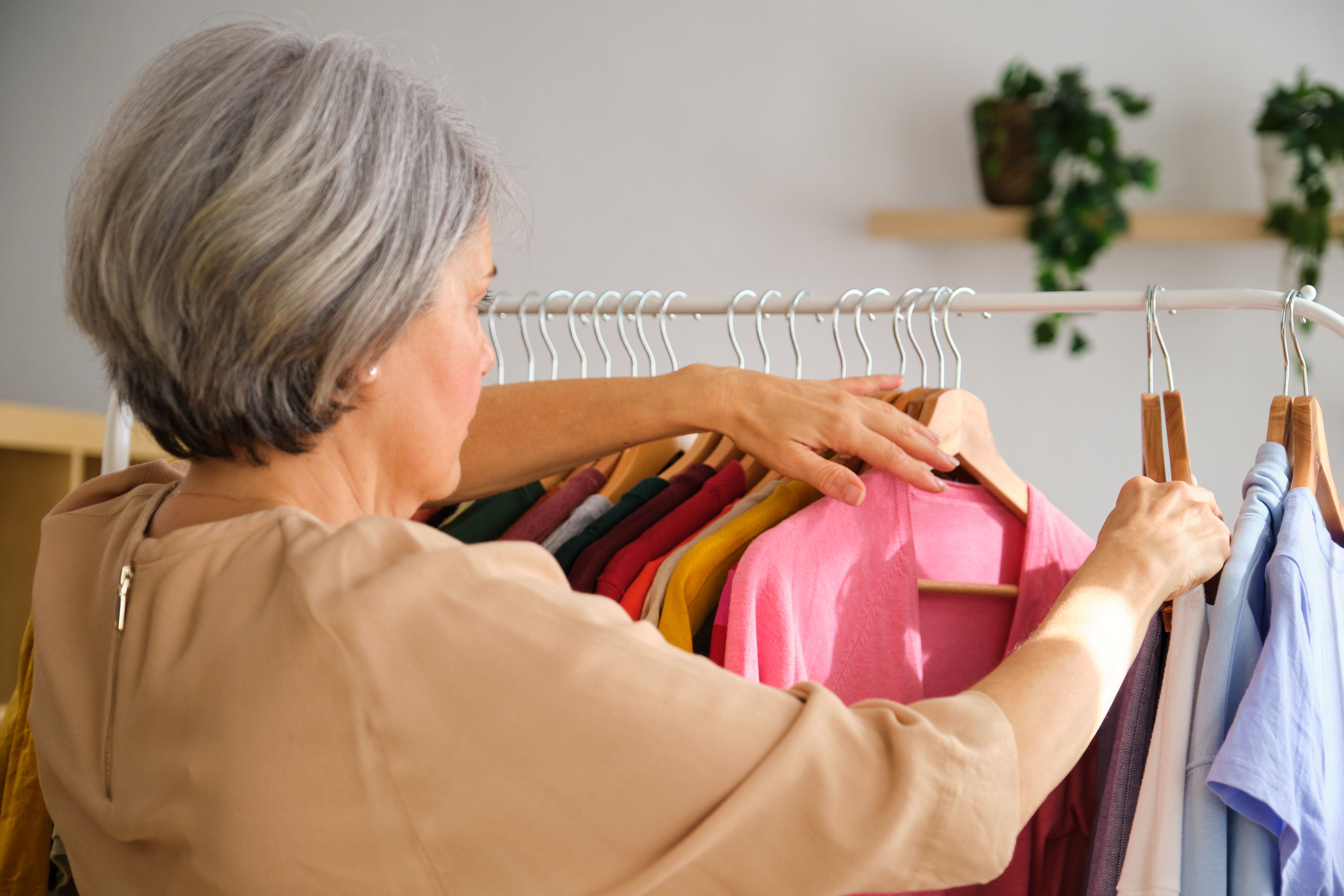 A mature woman is choosing the clothes she want to wear from hangers