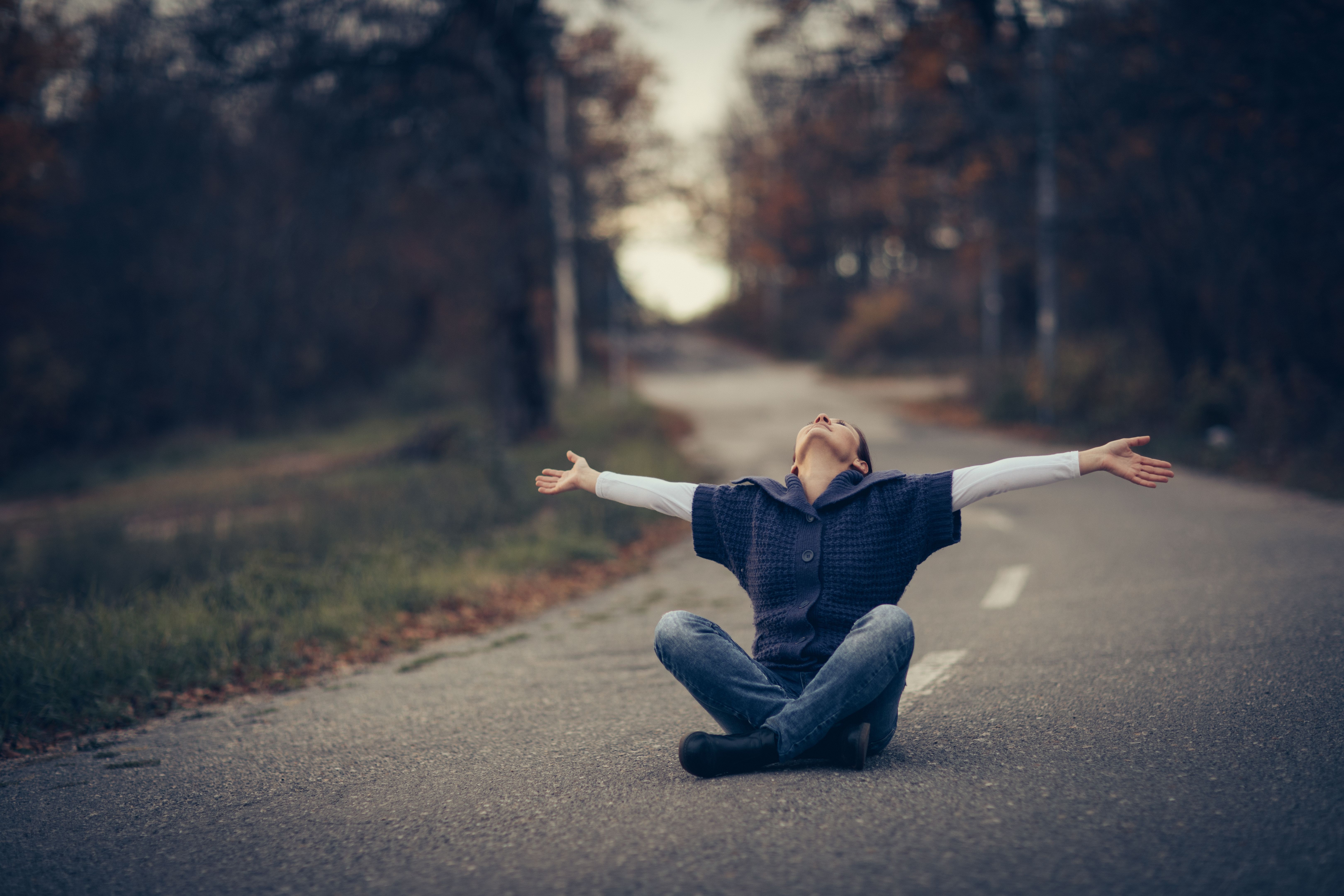 Young woman sitting on asphalt forest road
