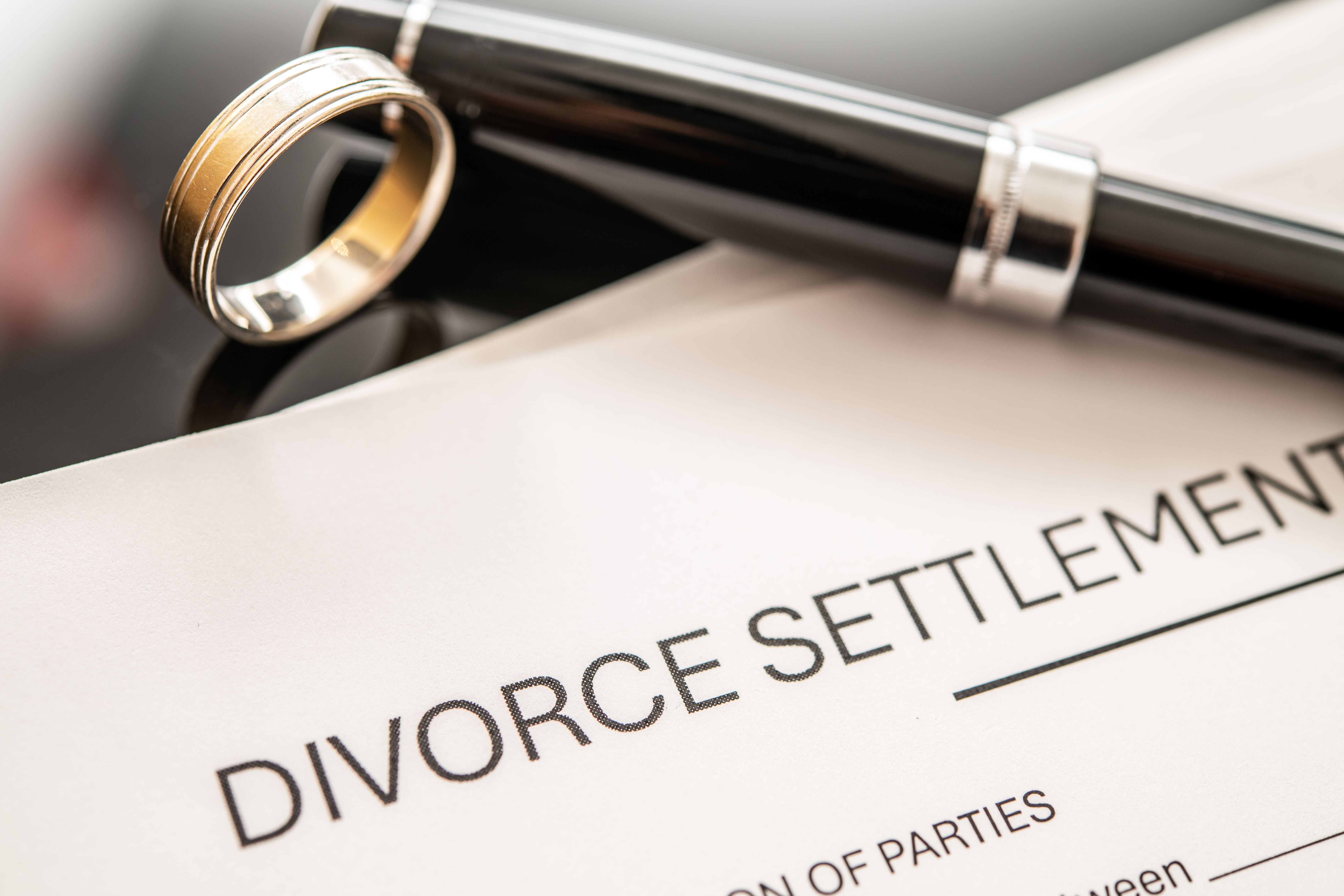 Divorce Settlement Agreement Document with Wedding Ring and Pen on Table Top for Legal and Financial Context in Family Law