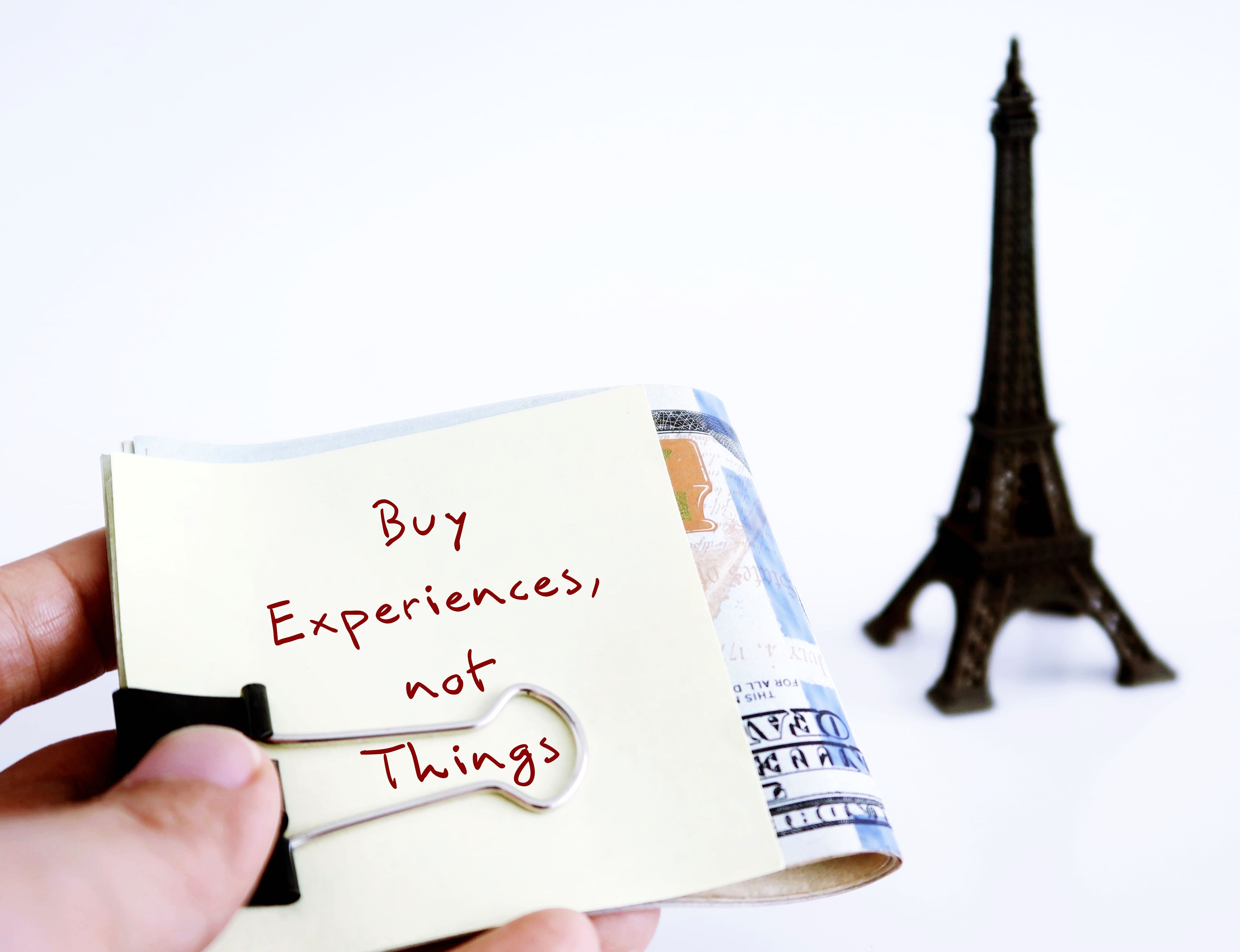 Hand holding cash money on Eiffel background with note written BUY EXPERIENCES, NOT THINGS means money can buy satisfaction from experiential purchases - travel, entertainment - than material buying