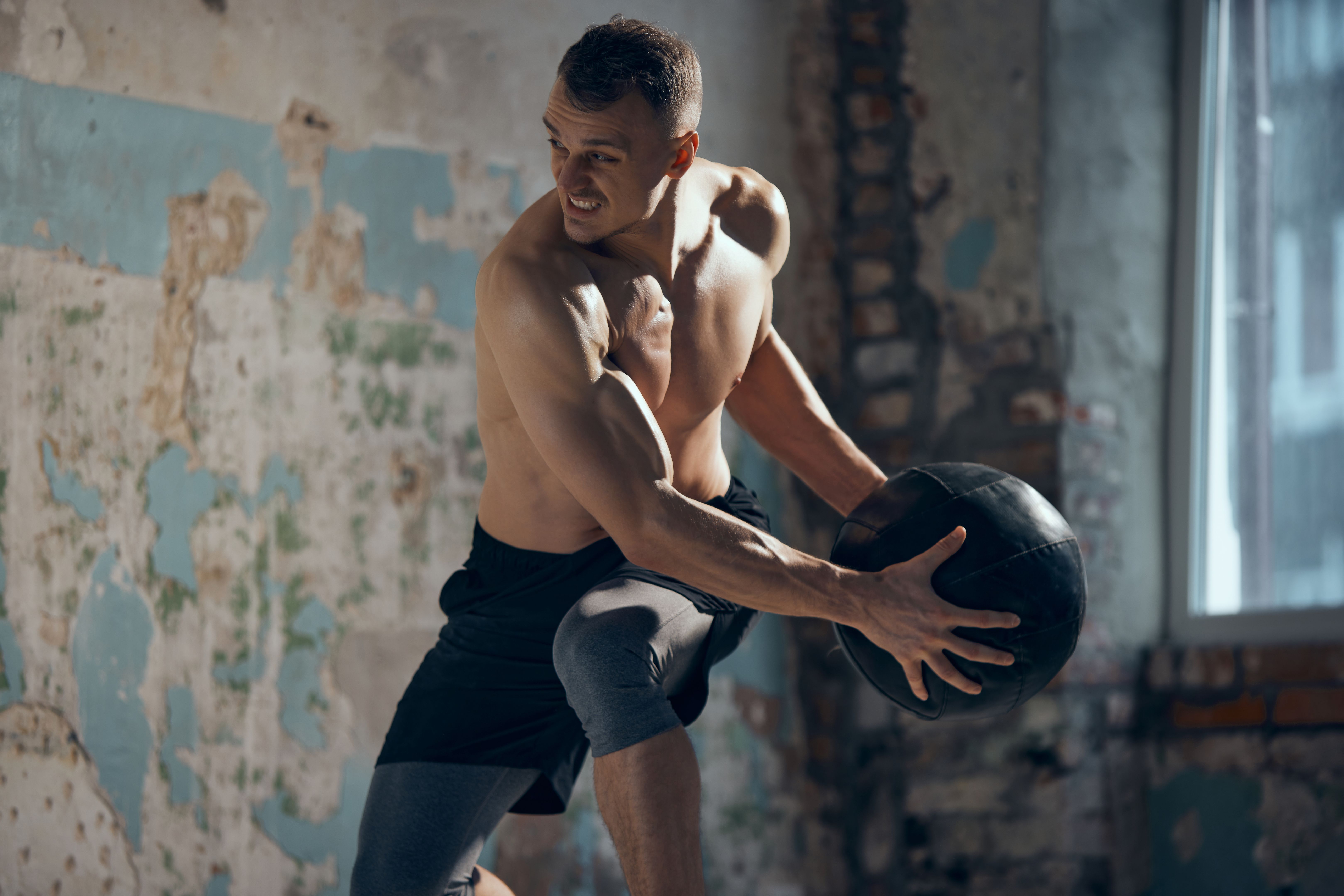 Full body workout. Young muscular man with strong, relief body shape training shirtless with fitness ball indoors. Sweat body. Concept of sportive lifestyle