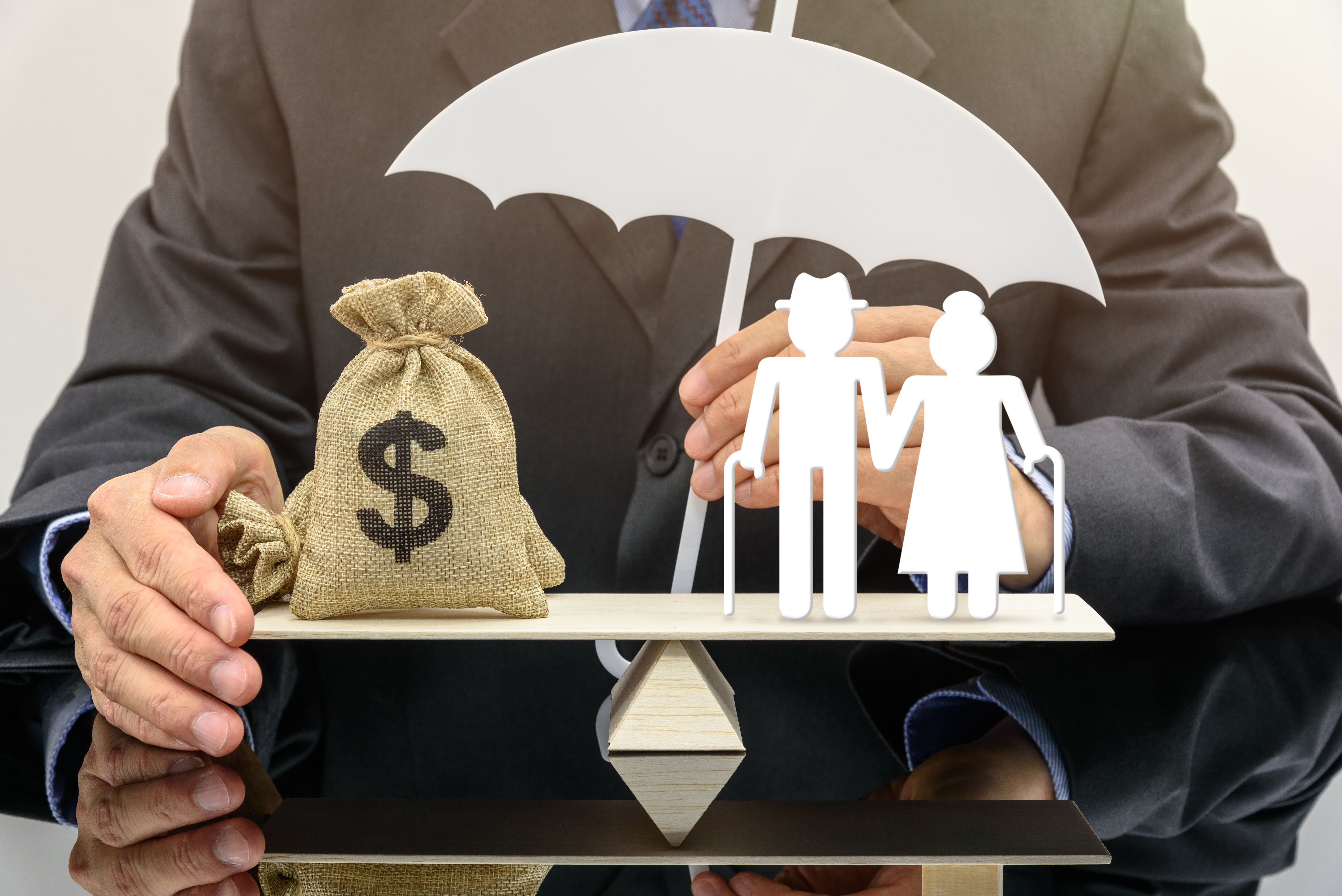 Pension insurance for retirees and social security tax, financial concept : Senior or elder retired couple stands on a seesaw or a balance scale with a US dollar bag, under a protection from insurer.