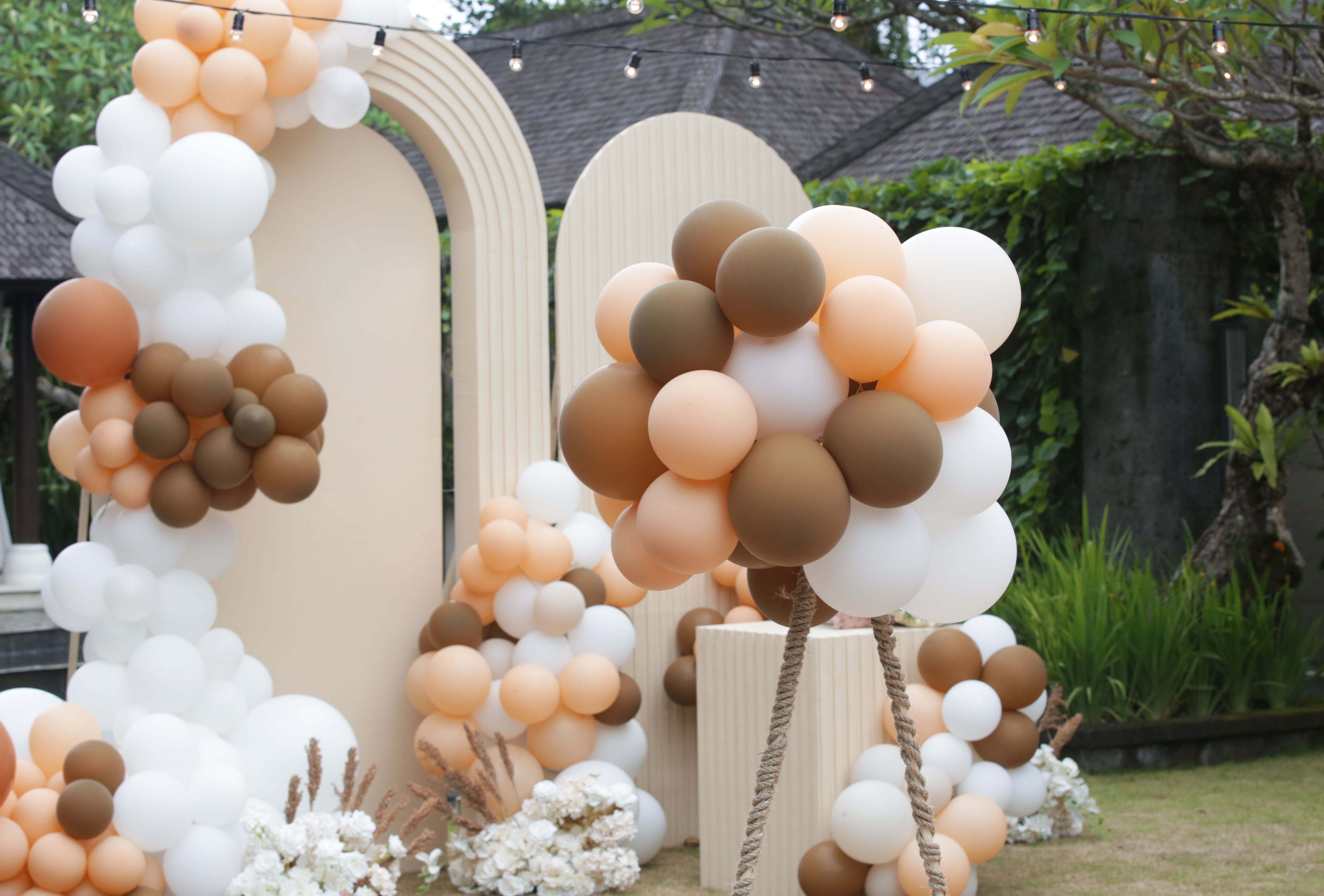 Creative gender neutral baby shower or birthday decoration in the garden. Bohemian style outdoor event set up with balloons. White cream peach caramel balloon arch kit.