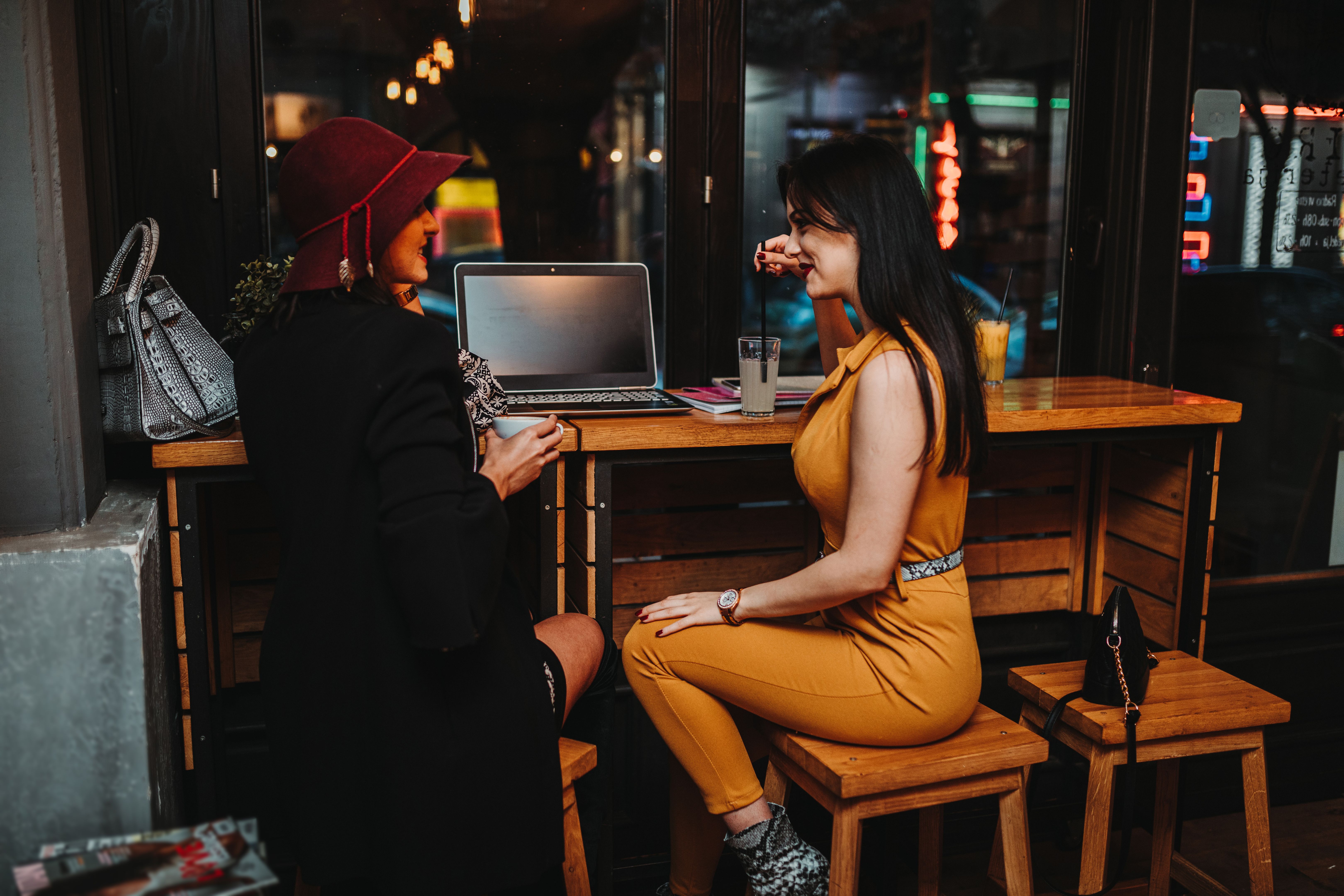 Two young woman sitting in coffee bar and using laptop