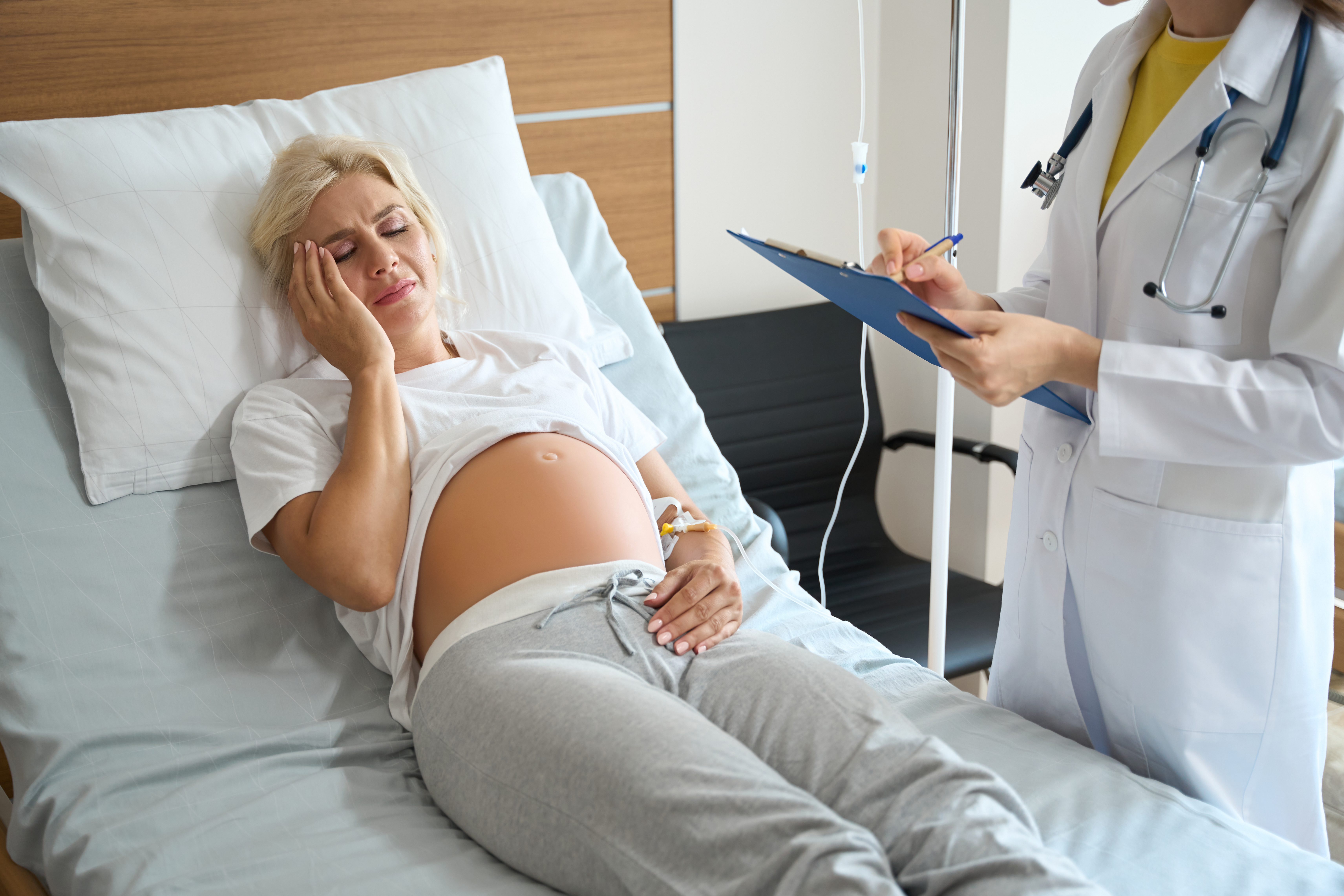Doctor writing in clipboard of pregnant woman with head pain while checking her