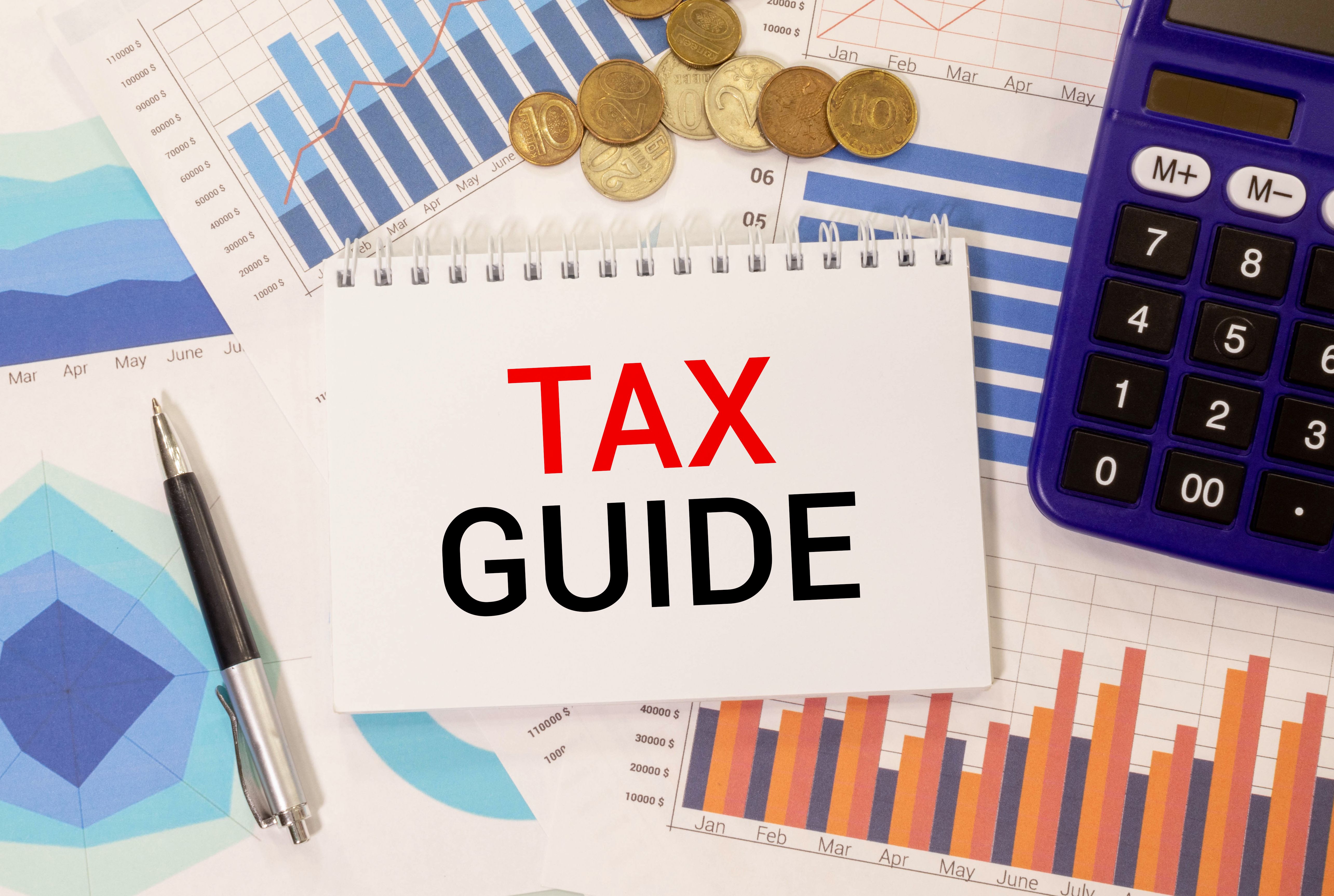 Calculator with text Tax Guide. Calculator, currency, book, bills and computer keyboard on bright background.