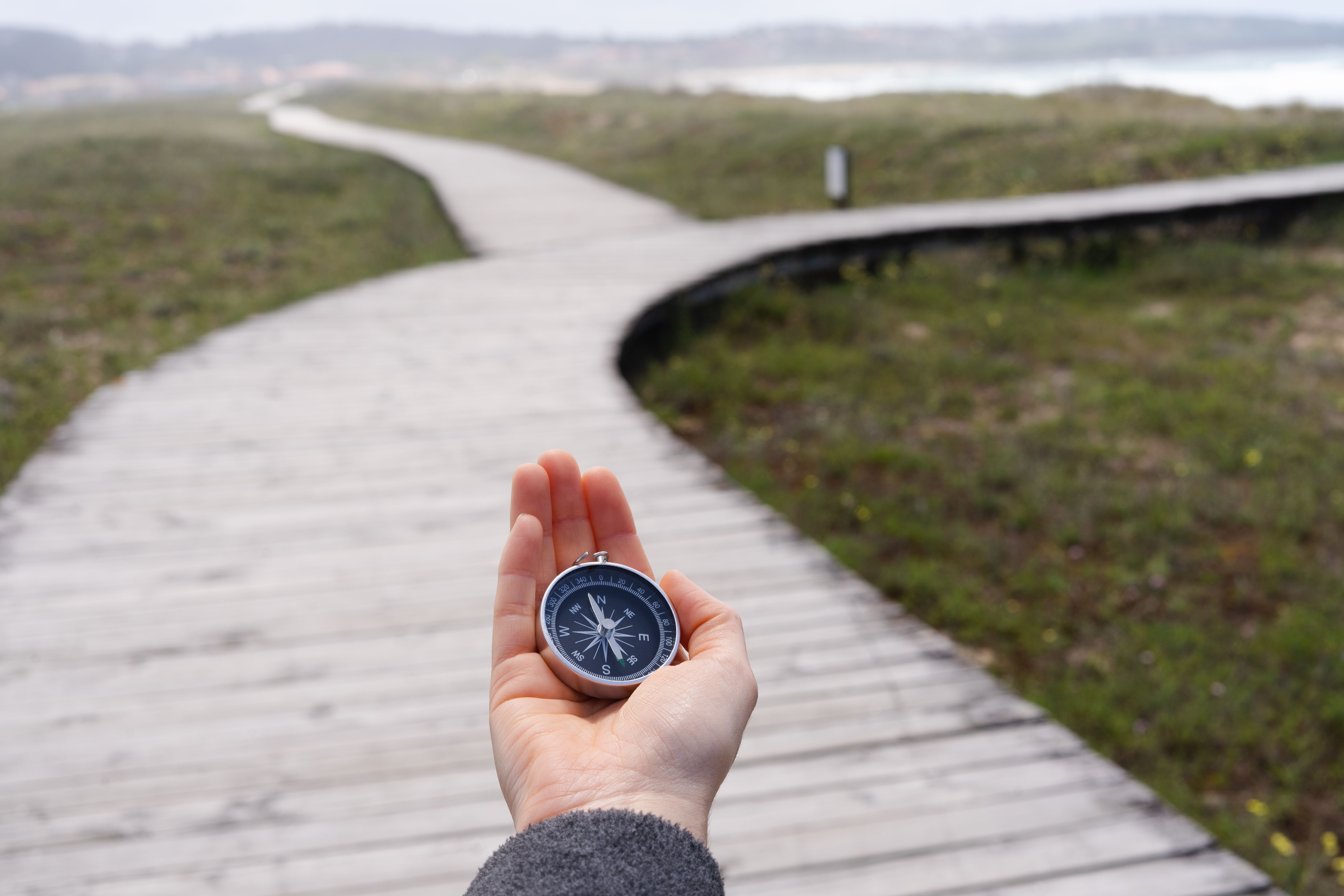 A person holding a compass on a wooden boardwalk.
