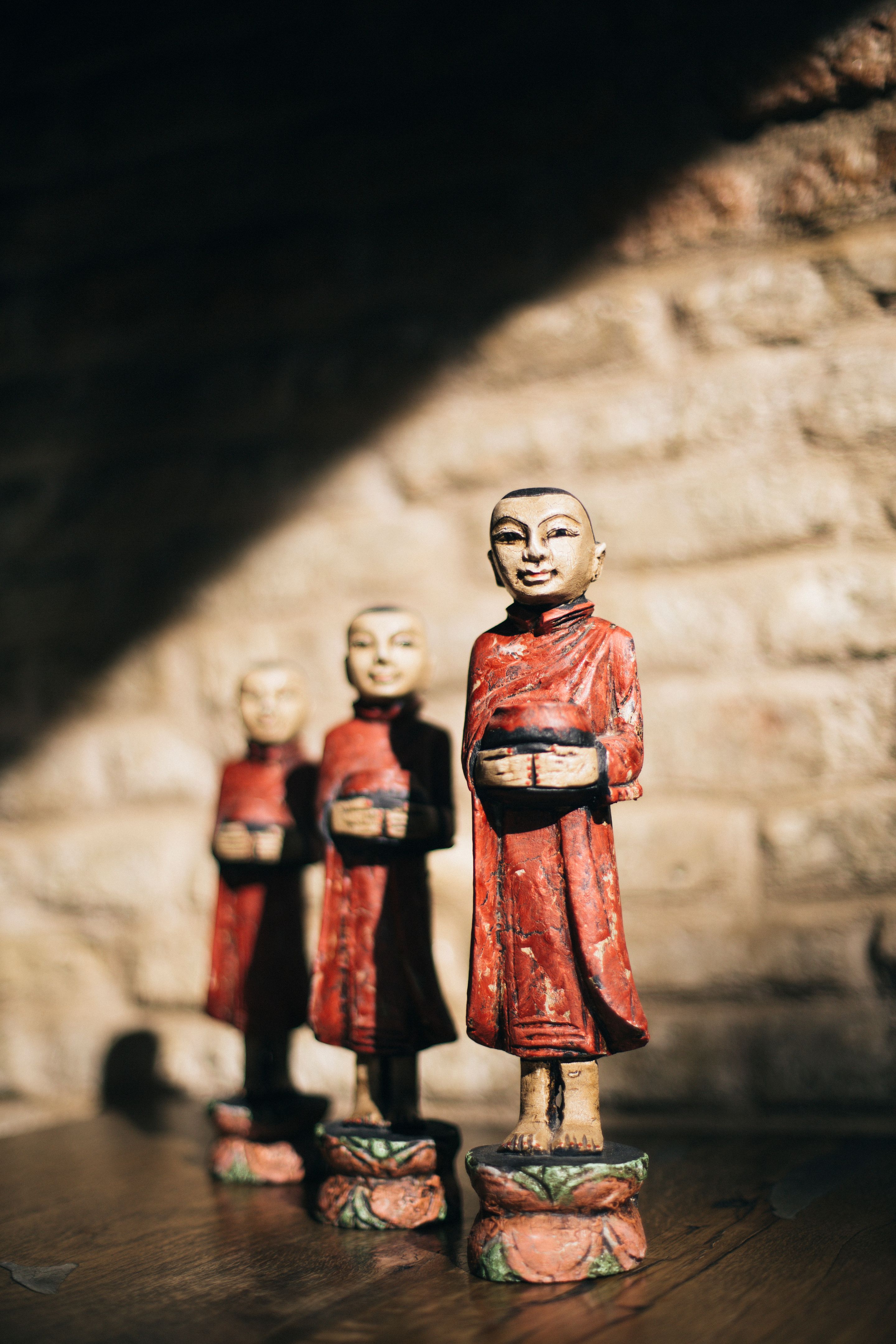 Traditional Thai monk statues holding alms bowls, Displayed against a rustic brick wall with warm sunlight, Cultural and spiritual decor for Thai restaurant ambiance and interior design