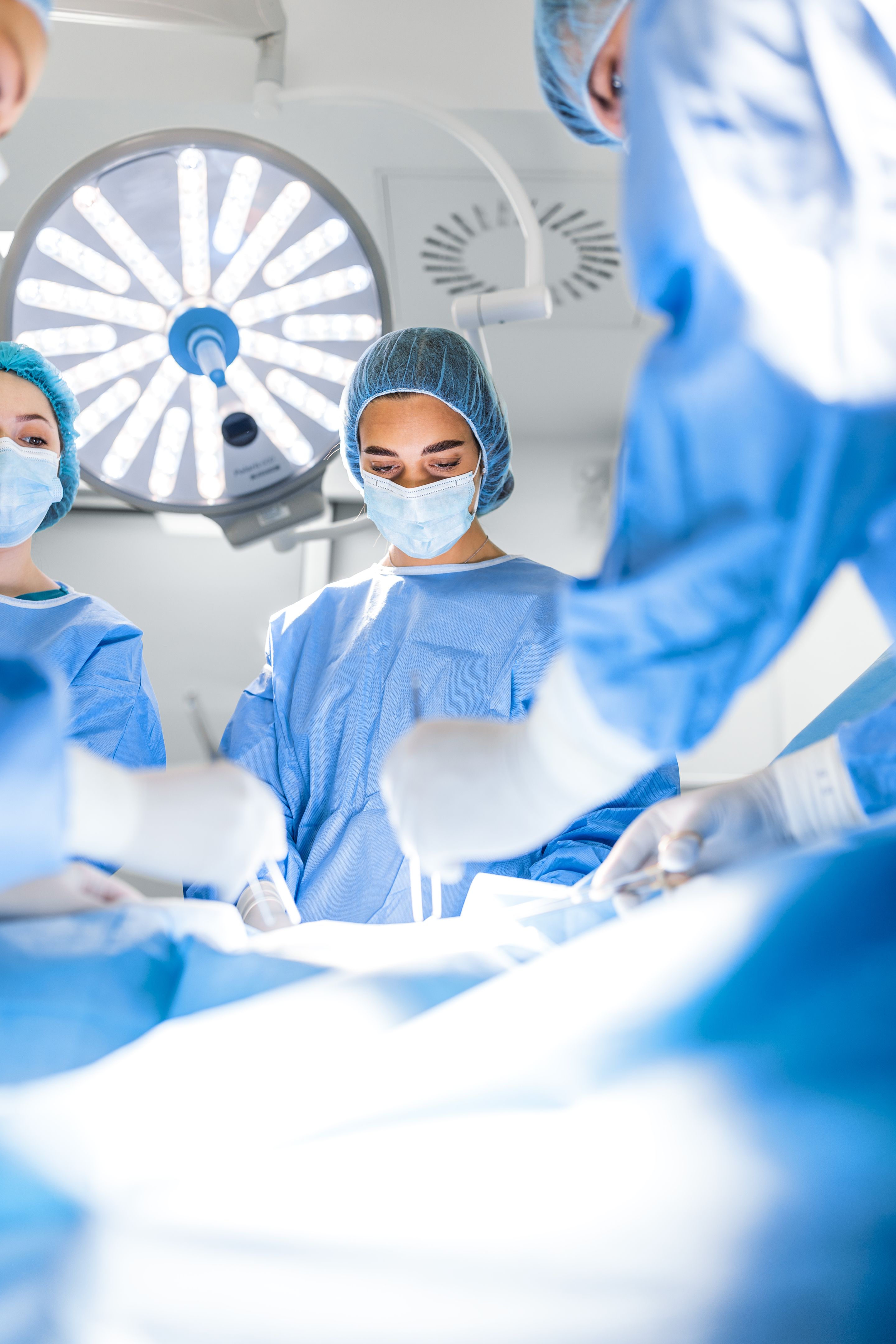 Preparation for the beginning of surgical operation with a cut. Group of surgeons at work in operating theater toned in blue. Medical team performing operation