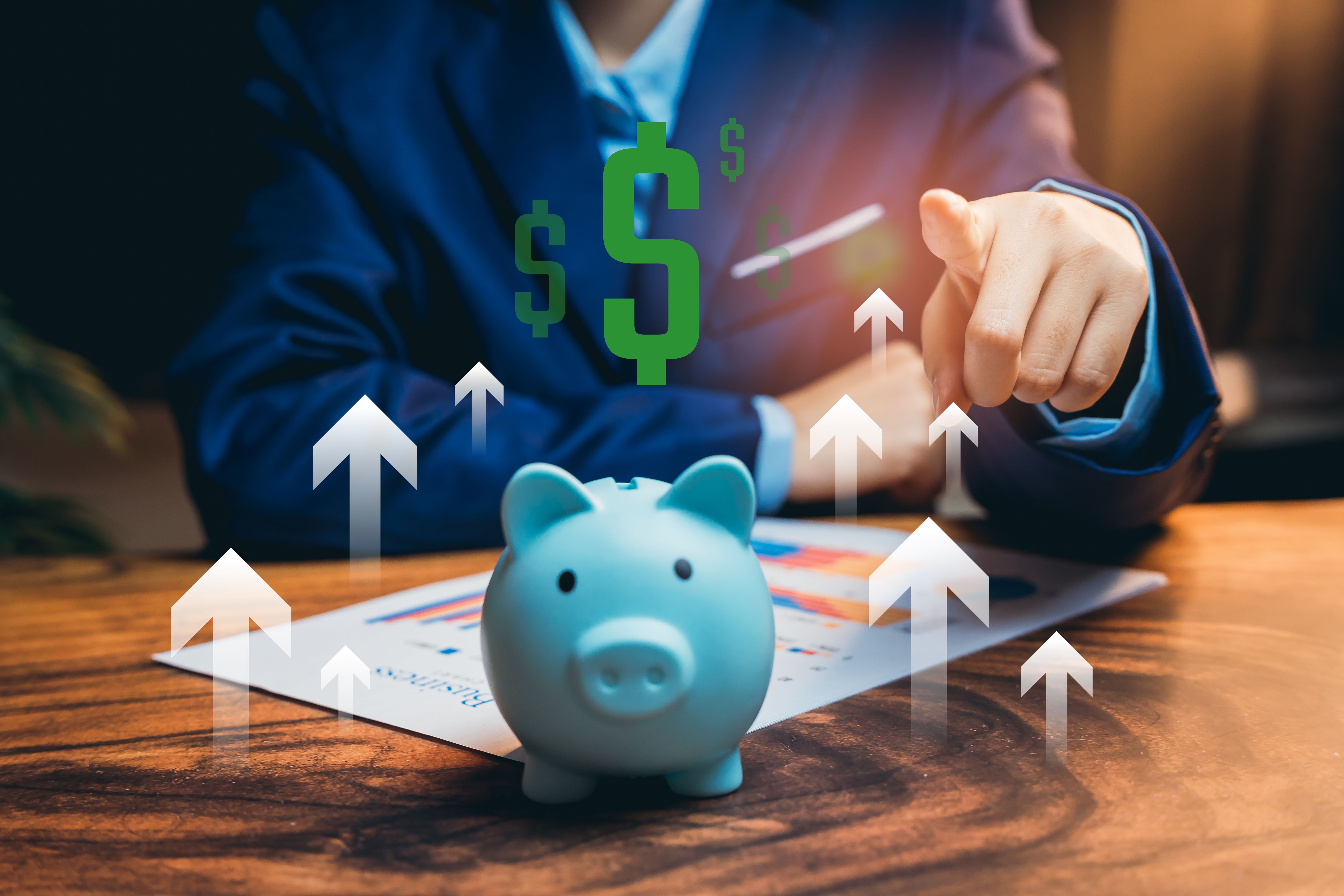 Saving money concept. Businessman in Suit Pointing to Rising Profit Graph with Piggy Bank on Table Illustrating Financial Success Concept