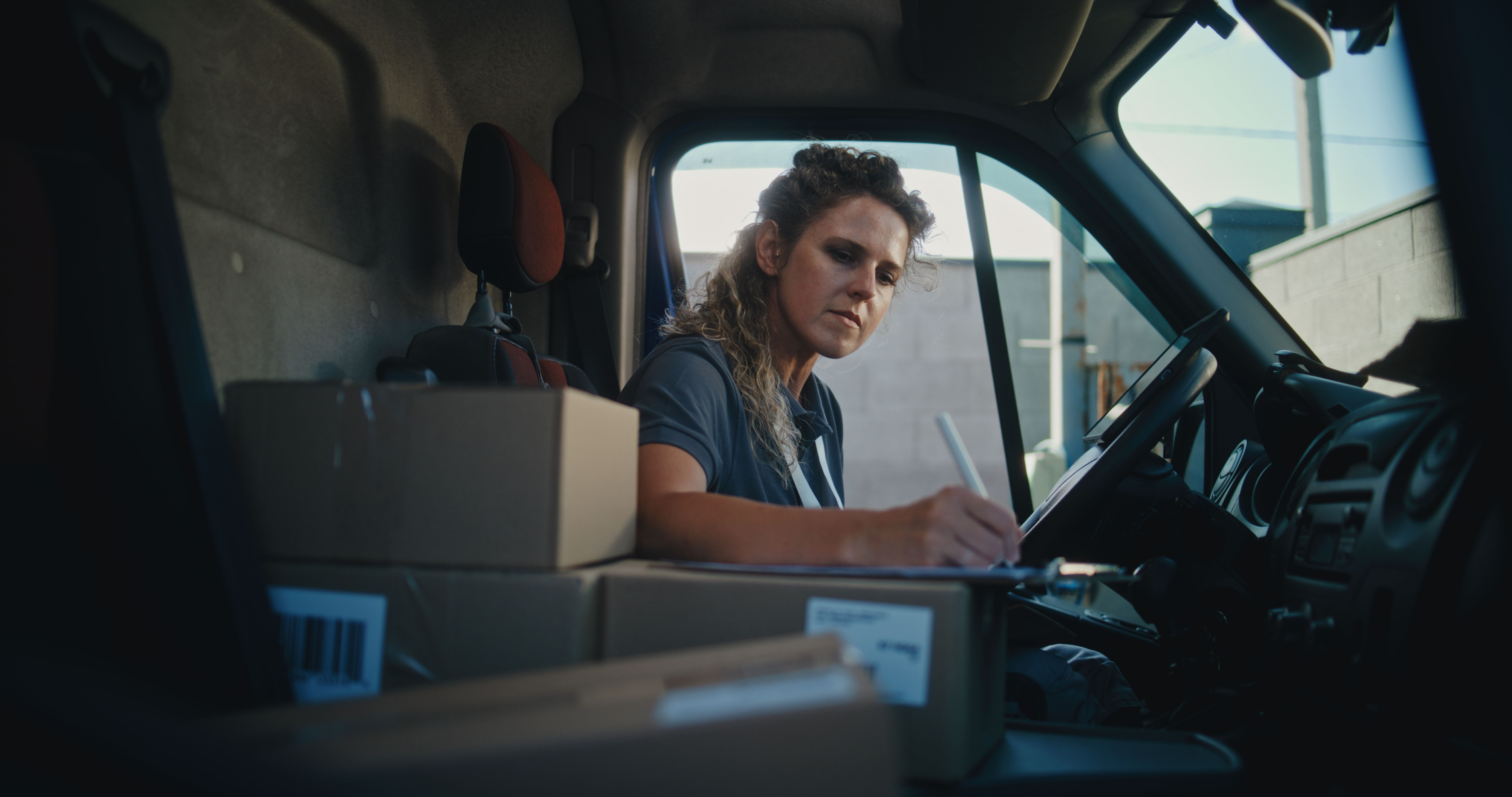 Female Product Supplier in Truck Talking by Phone, Using Digital Tablet, Filling Out Papers