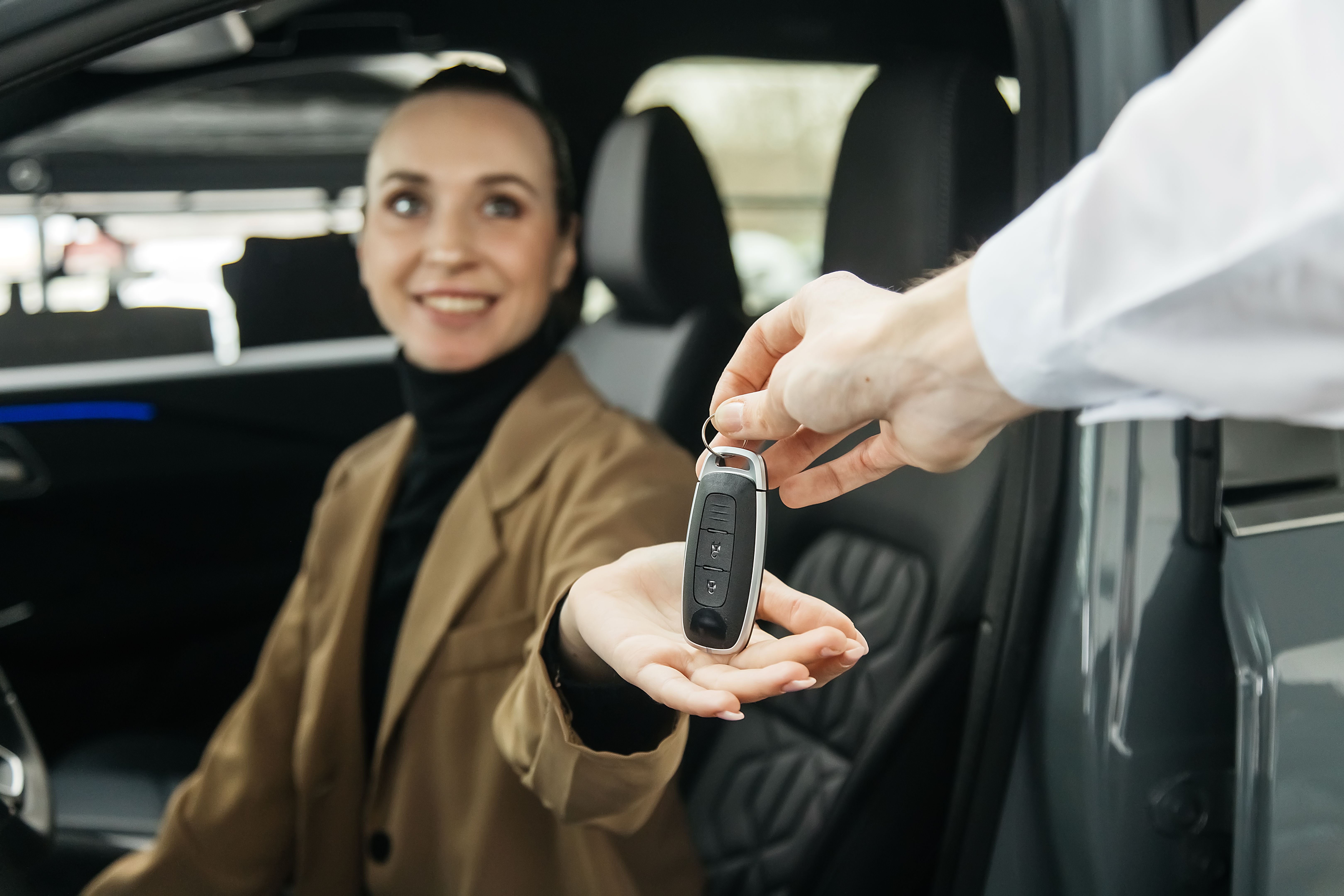 The car dealer hands the car keys to a woman
