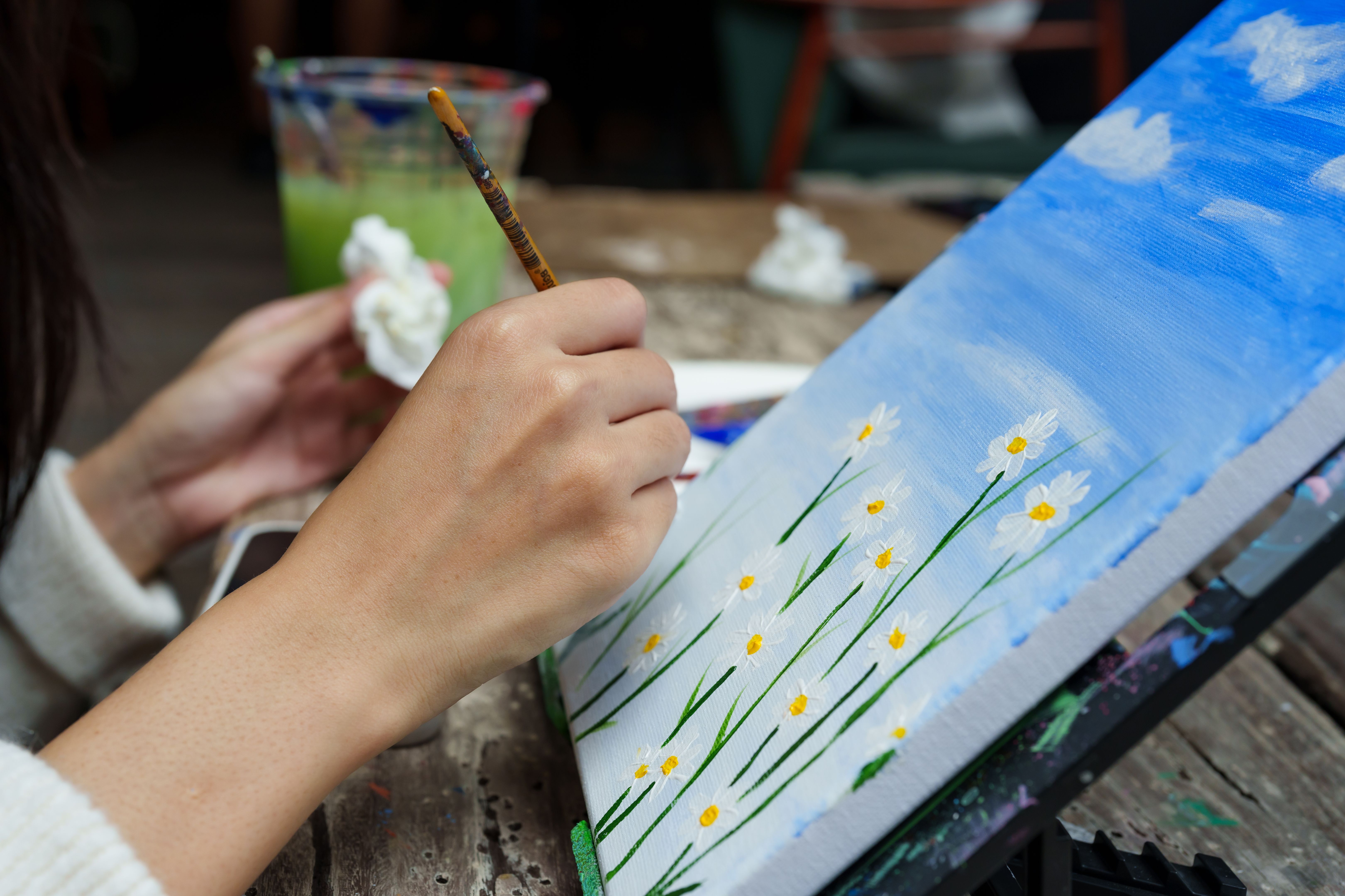 Close-up small paintbrush with yellow paint on paintbrush, painter's hand holding handle firmly, dip into center where there is white flower petal that is daisy, poke slowly make it look beautiful. Close-up small paintbrush with yellow paint on paintbrush, painter's hand holding handle firmly, dip into center where there is white flower petal that is daisy, poke slowly make it look beautiful.