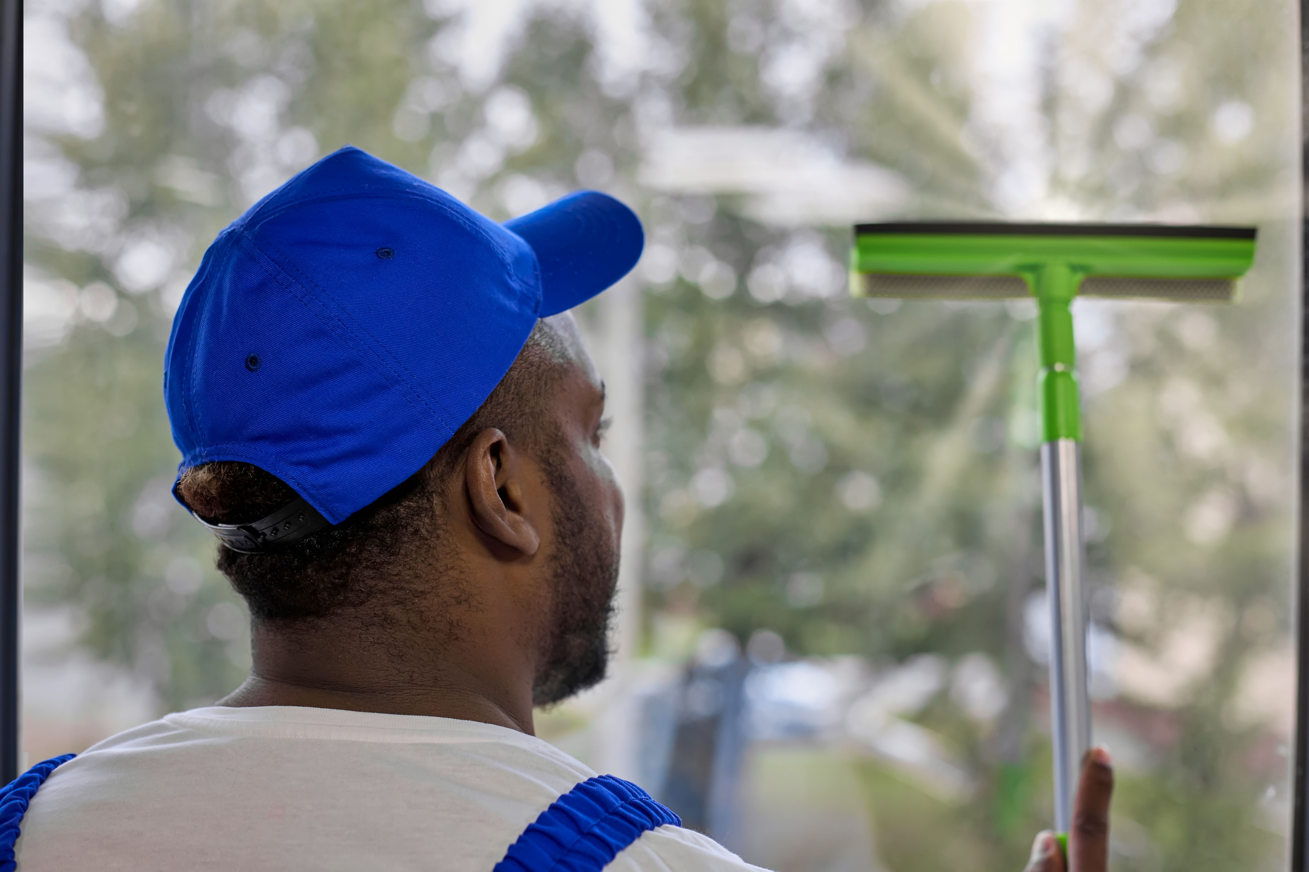 Strong African-American man in white T-shirt and cap with window cleaning brush
