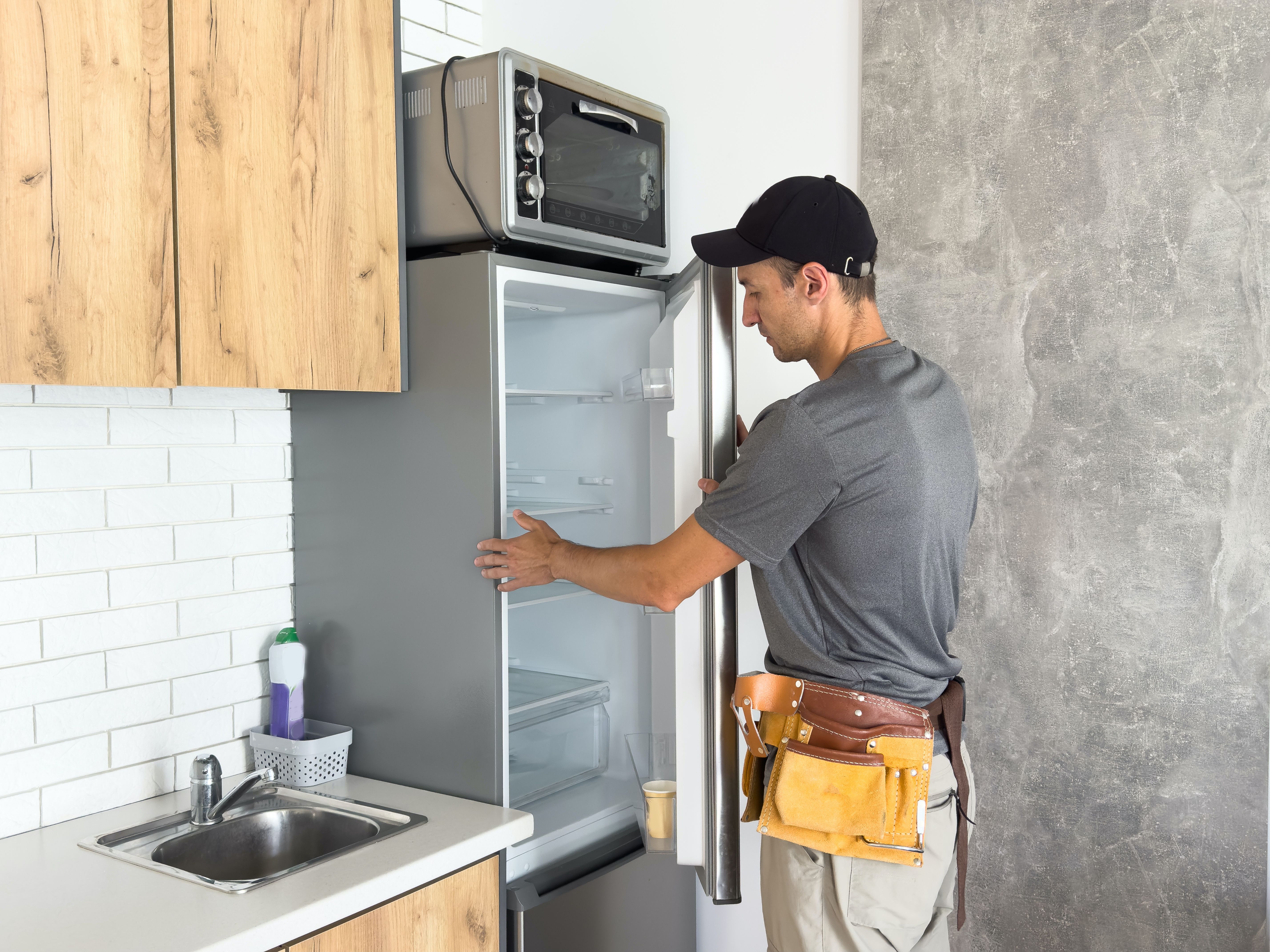 Male technician with screwdriver repairing refrigerator indoors