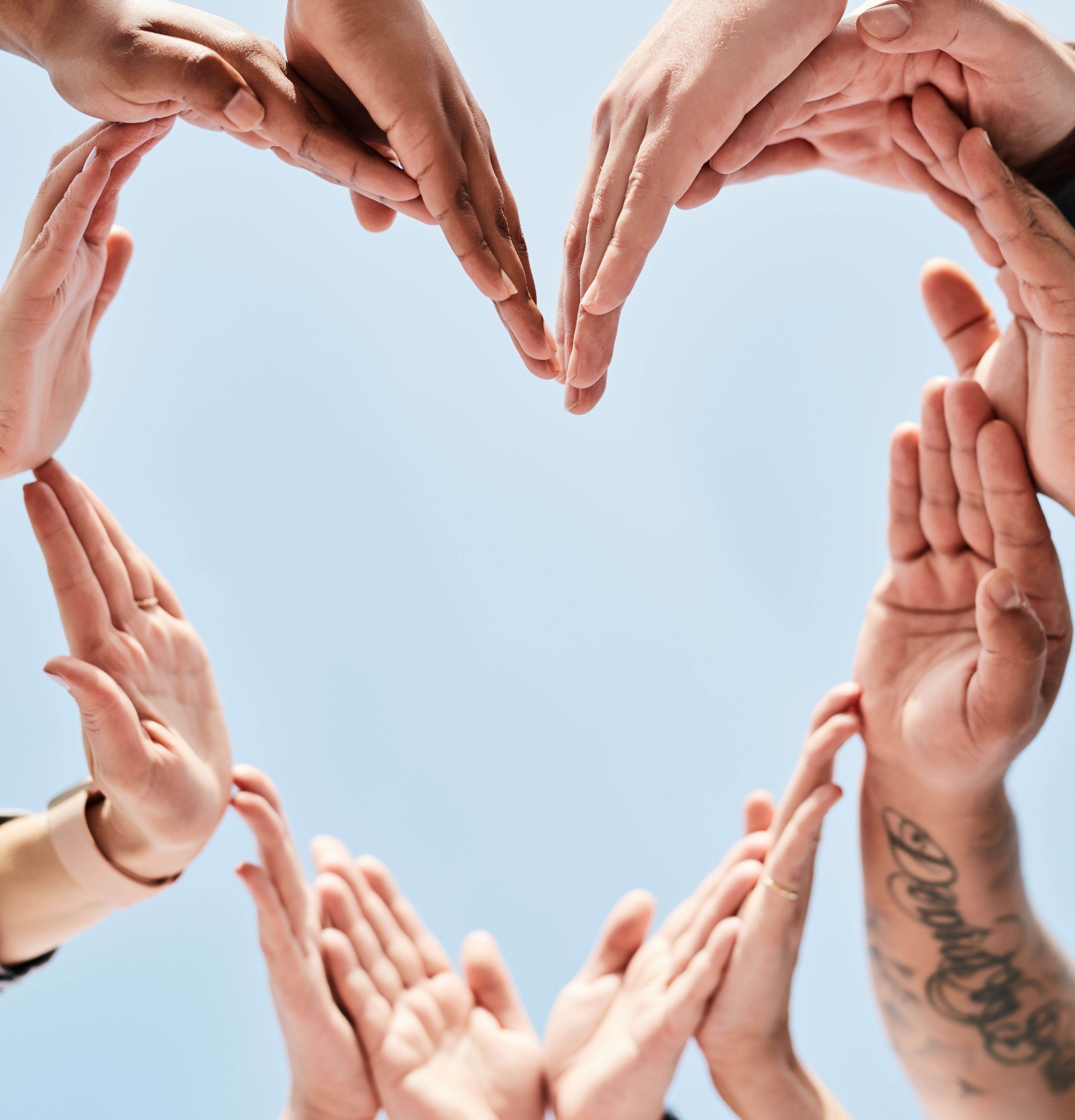 People, hands and unity forming heart in support, collaboration or teamwork below a blue sky background. Hand of group touching in hearty shape love symbol in trust, community or team synergy outside
