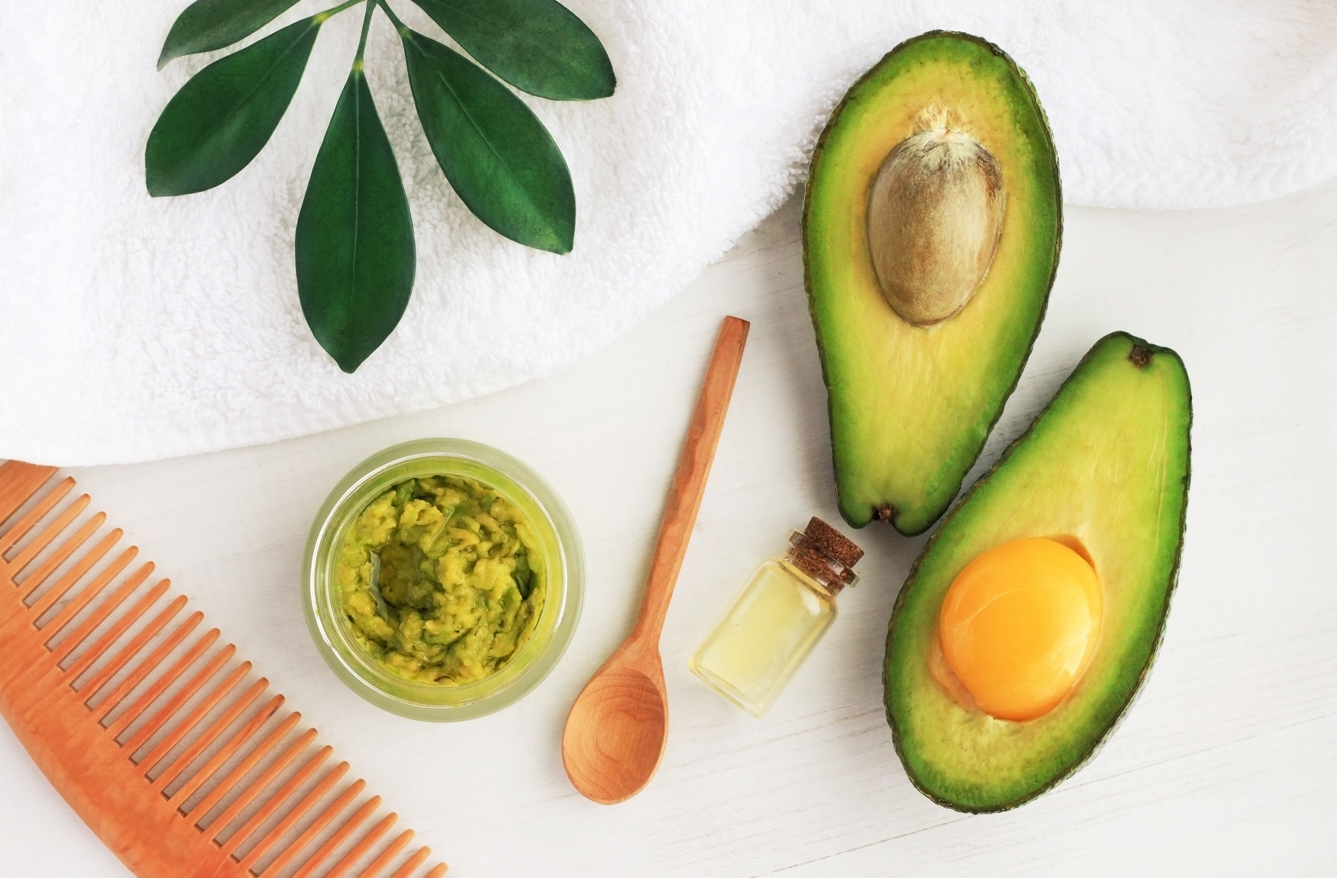 Making homemade hair mask with fresh green avocado and egg yolk ingredients top view white table