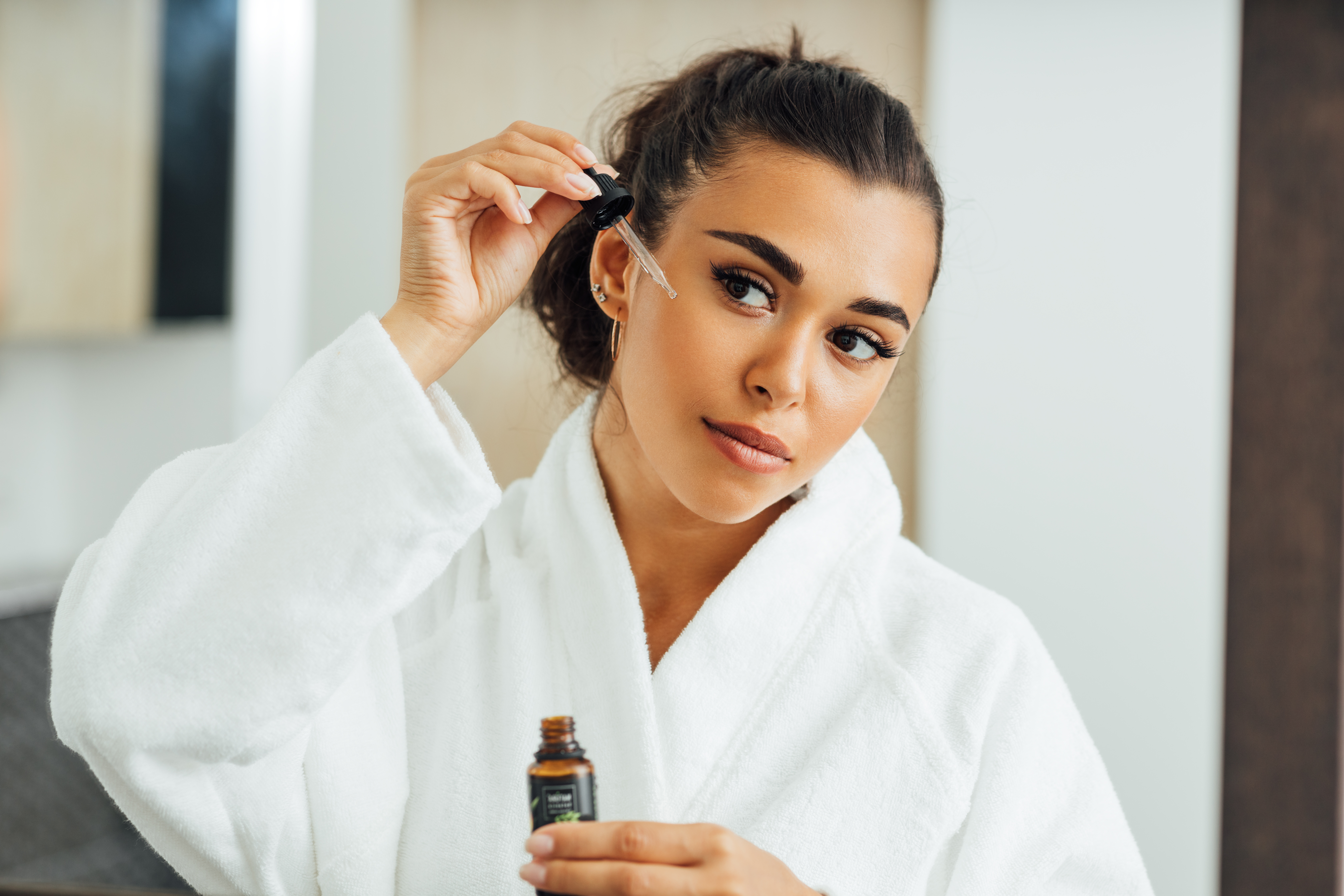 Beautiful woman using serum dropper in bathroom. Young female applying hyaluronic acid on her cheek. Beautiful woman using serum dropper in bathroom. Young female applying hyaluronic acid on her cheek.