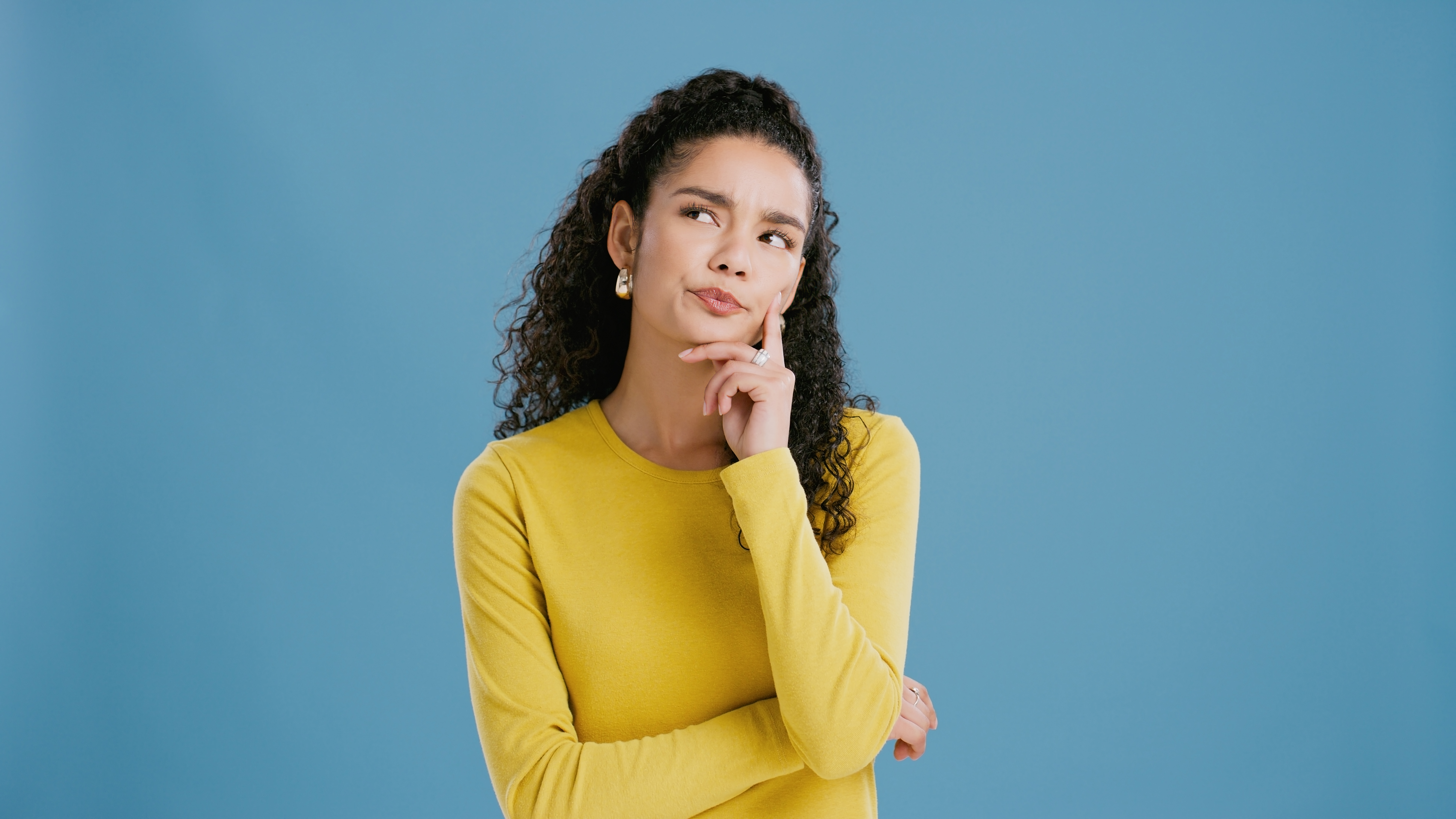 Woman, question and thinking in studio for confused mockup, planning and wonder or inspiration for solution. Brazilian model, doubt and option with emoji, ask and choice with idea by blue background
