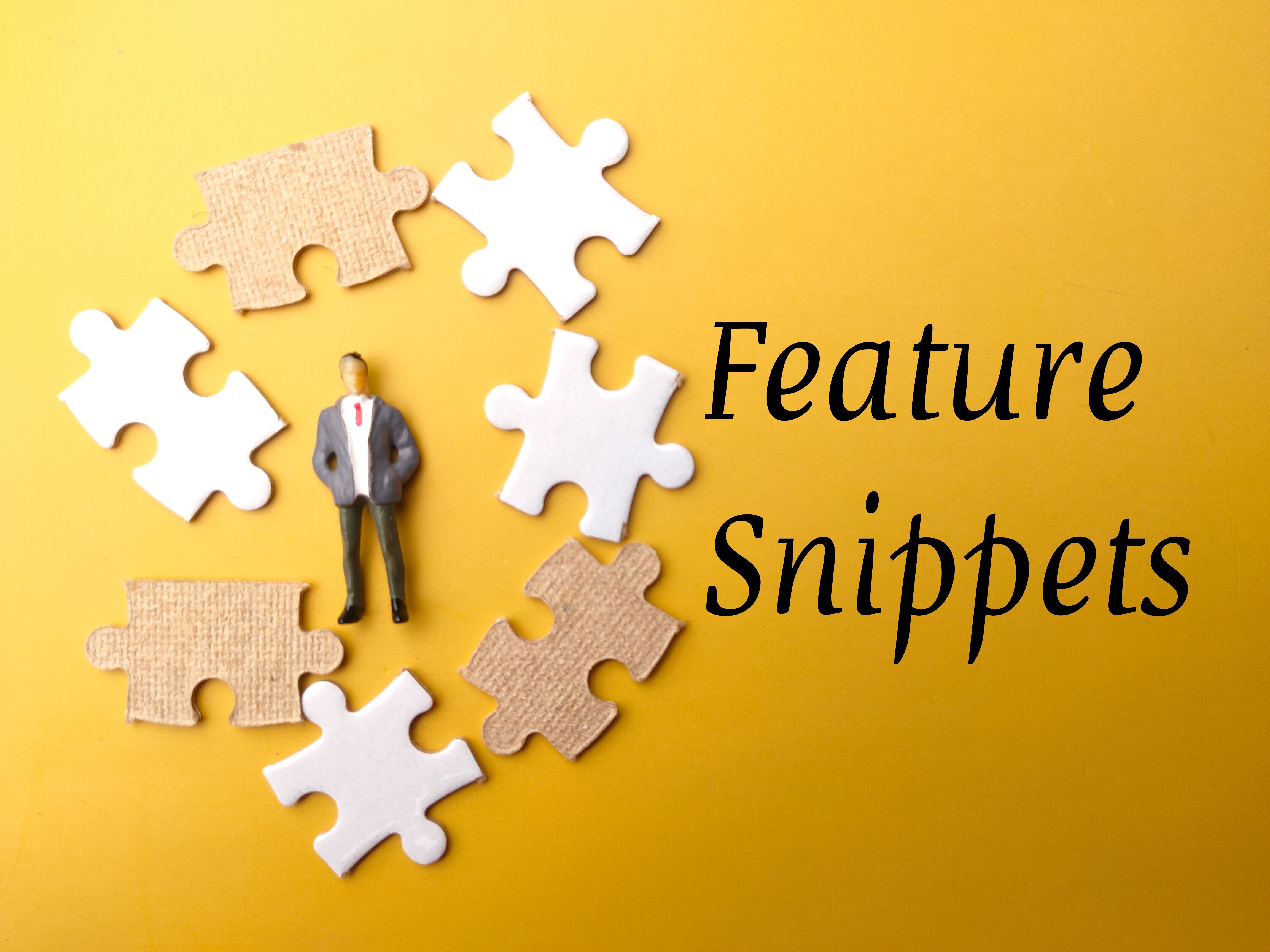 Miniature people and white puzzle with text Feature Snippets on a yellow background.