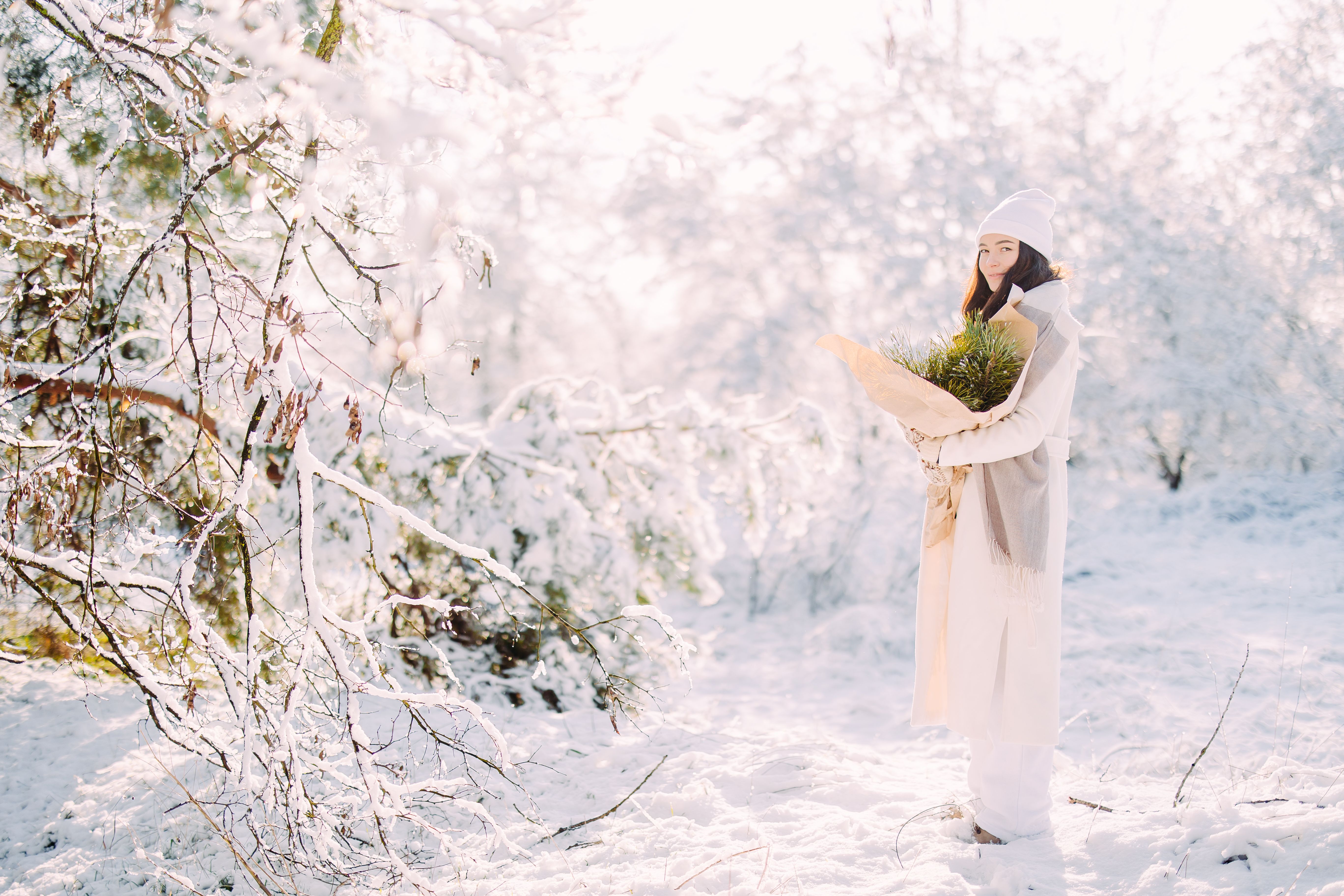 Happy young woman walks in forest among snow covered trees in sunny winter day.