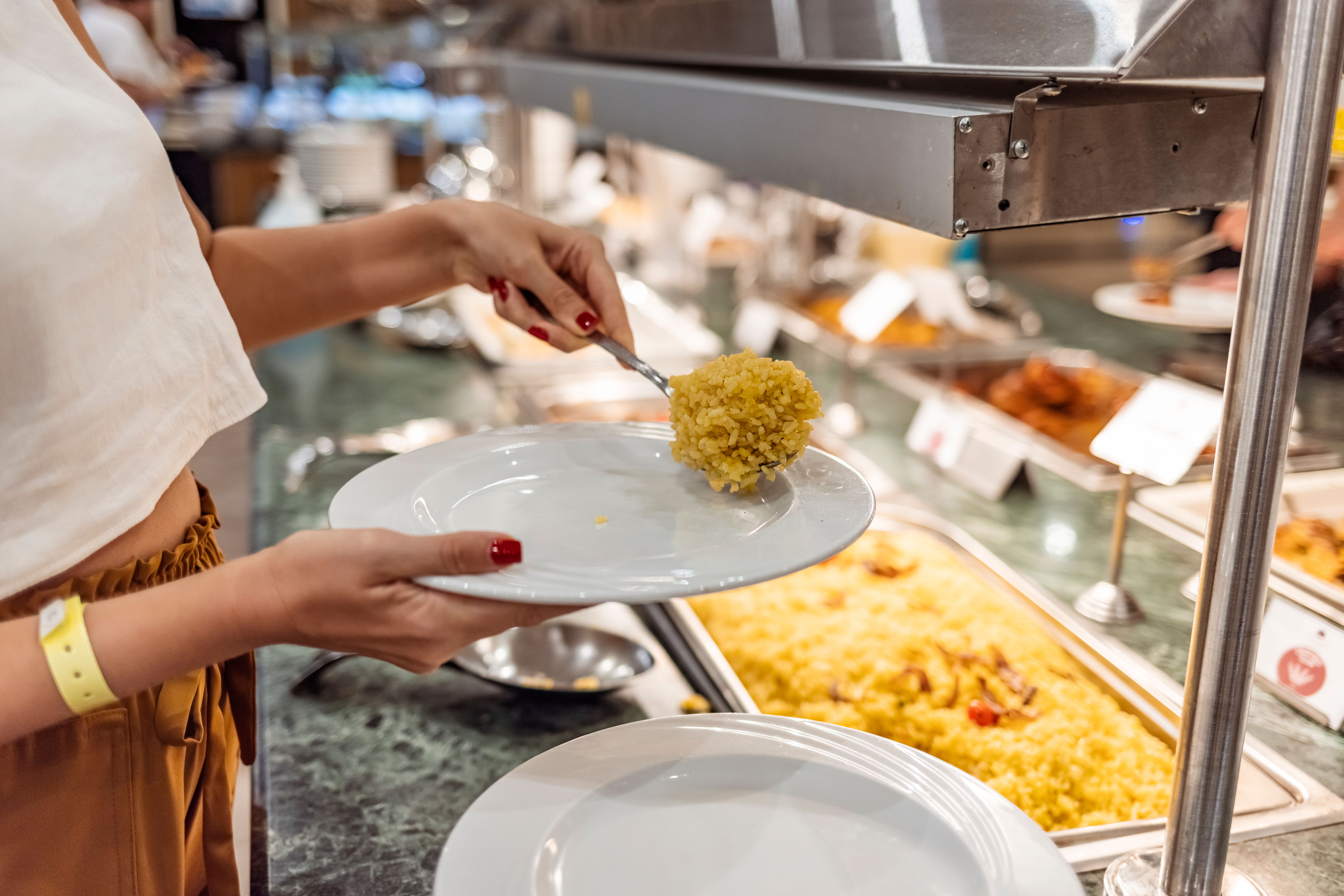 A hand picking up rice from open buffet in restaurant. A hand picking up rice from open buffet in restaurant.