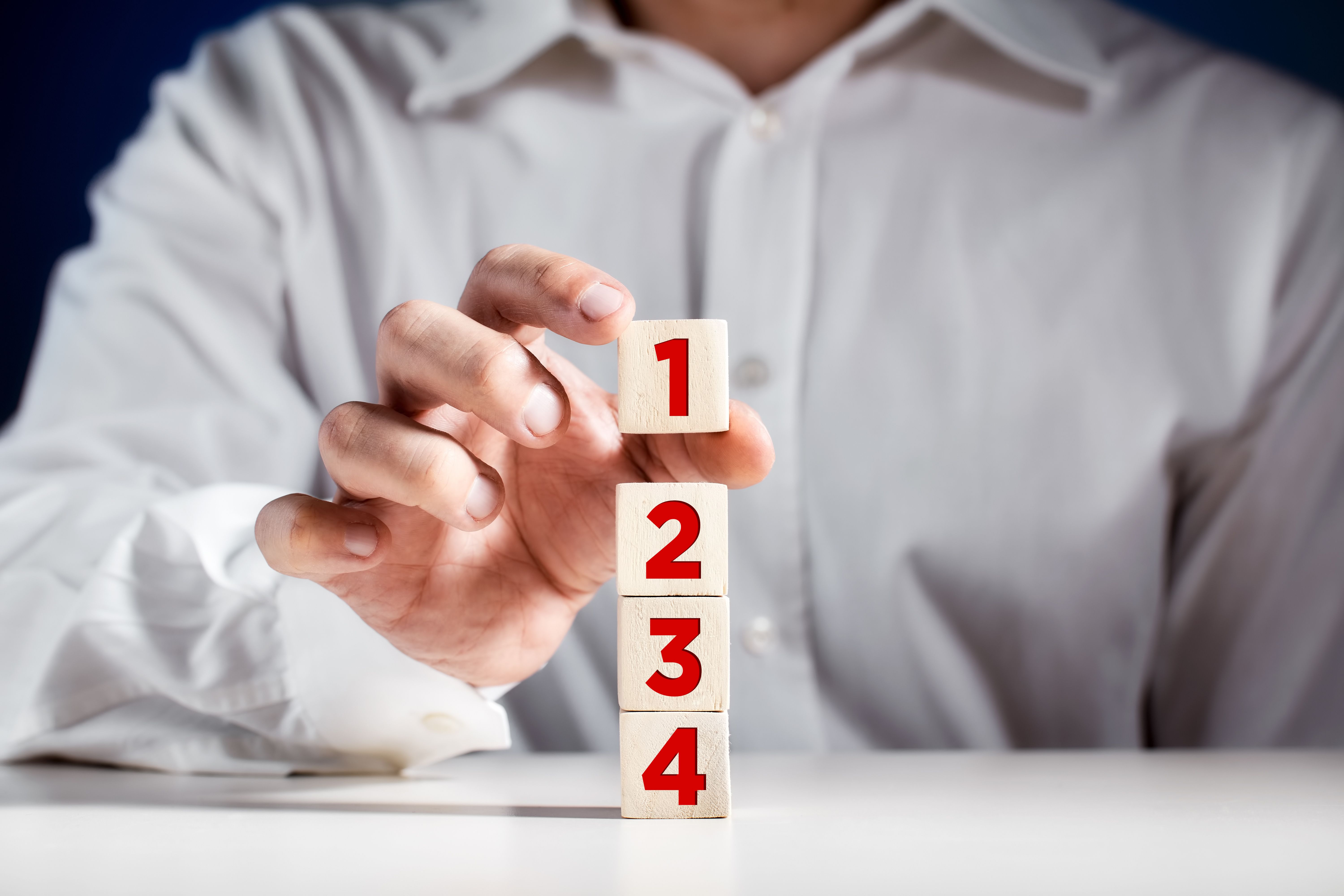 Businessman hand puts a wooden block with the number one on top of the tiered cubes. First step, level or rank Businessman hand puts a wooden block with the number one on top of the tiered cubes. First step, level or rank