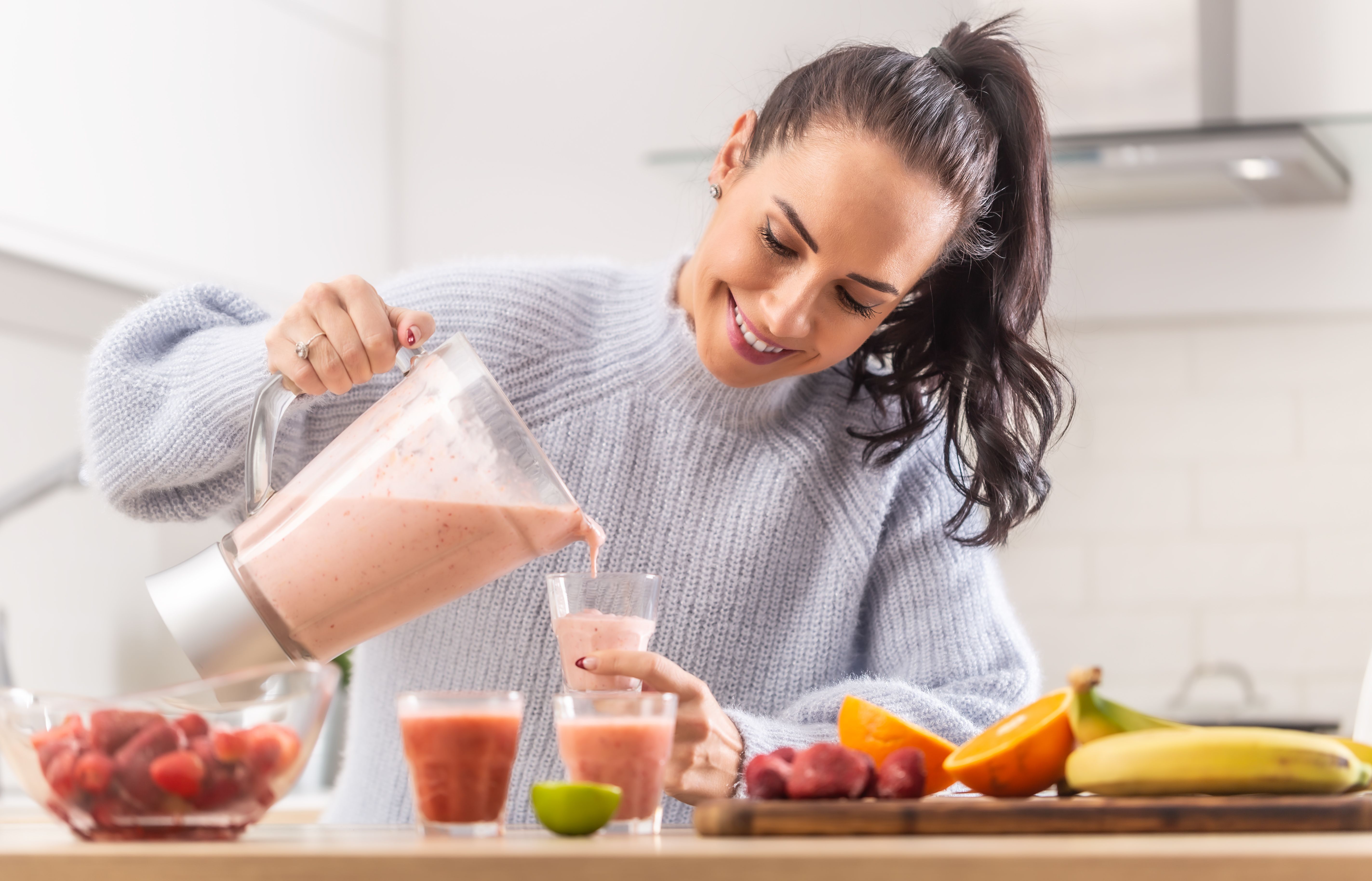 Woman pours fruit smoothie into cups in a kitchen. Woman pours fruit smoothie into cups in a kitchen.