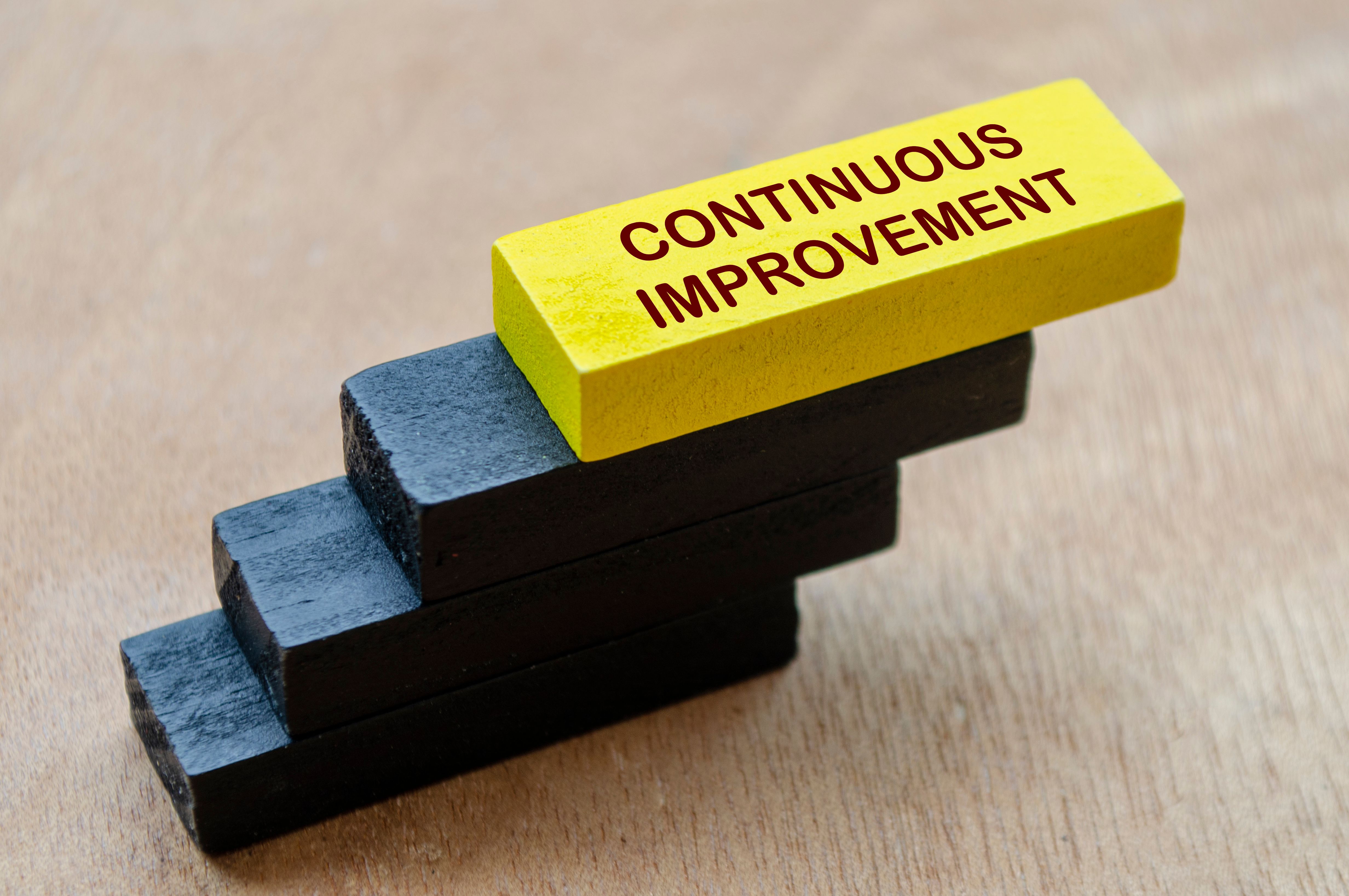Continuous Improvement text on yellow wooden block stacking on other black wooden blocks. Continuous Improvement concept.