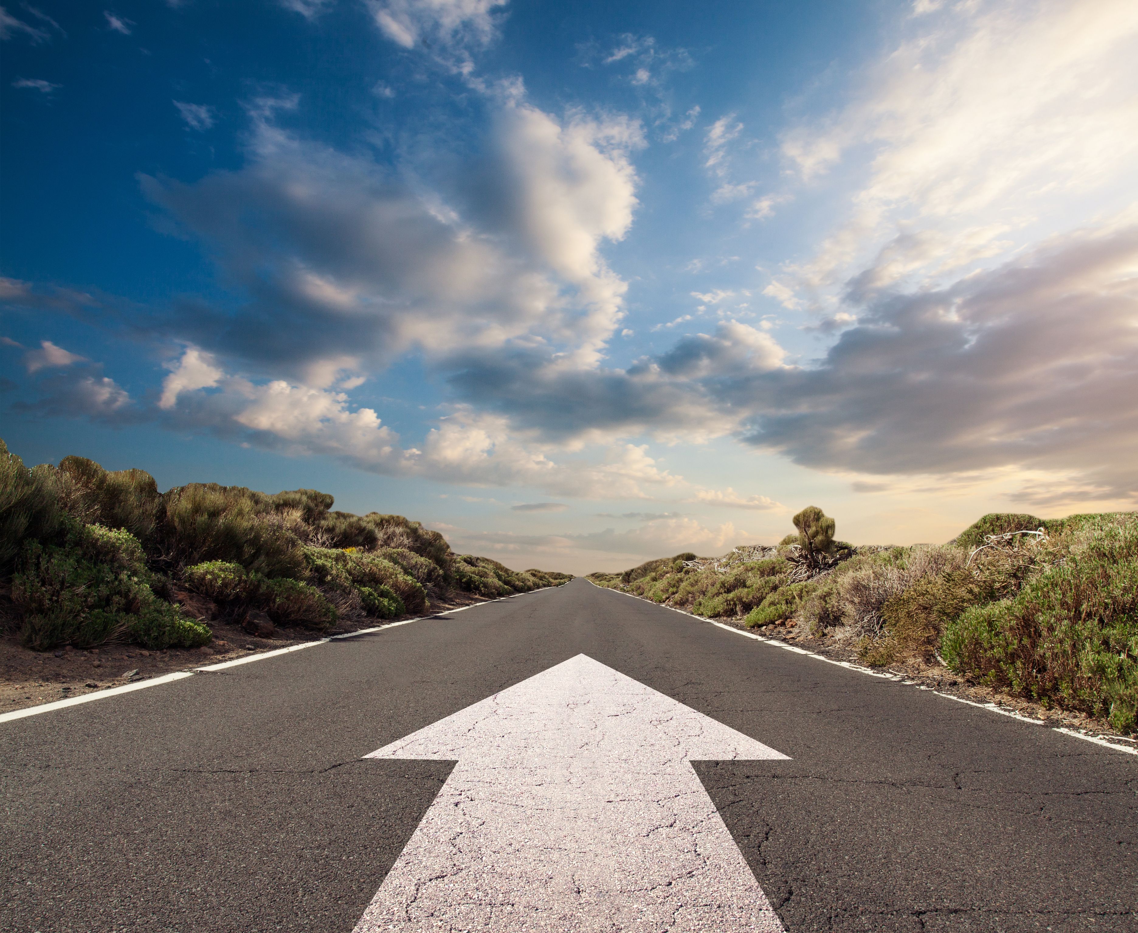 Blue sky with clouds and country road with white arrow Blue sky with clouds and country road with white arrow