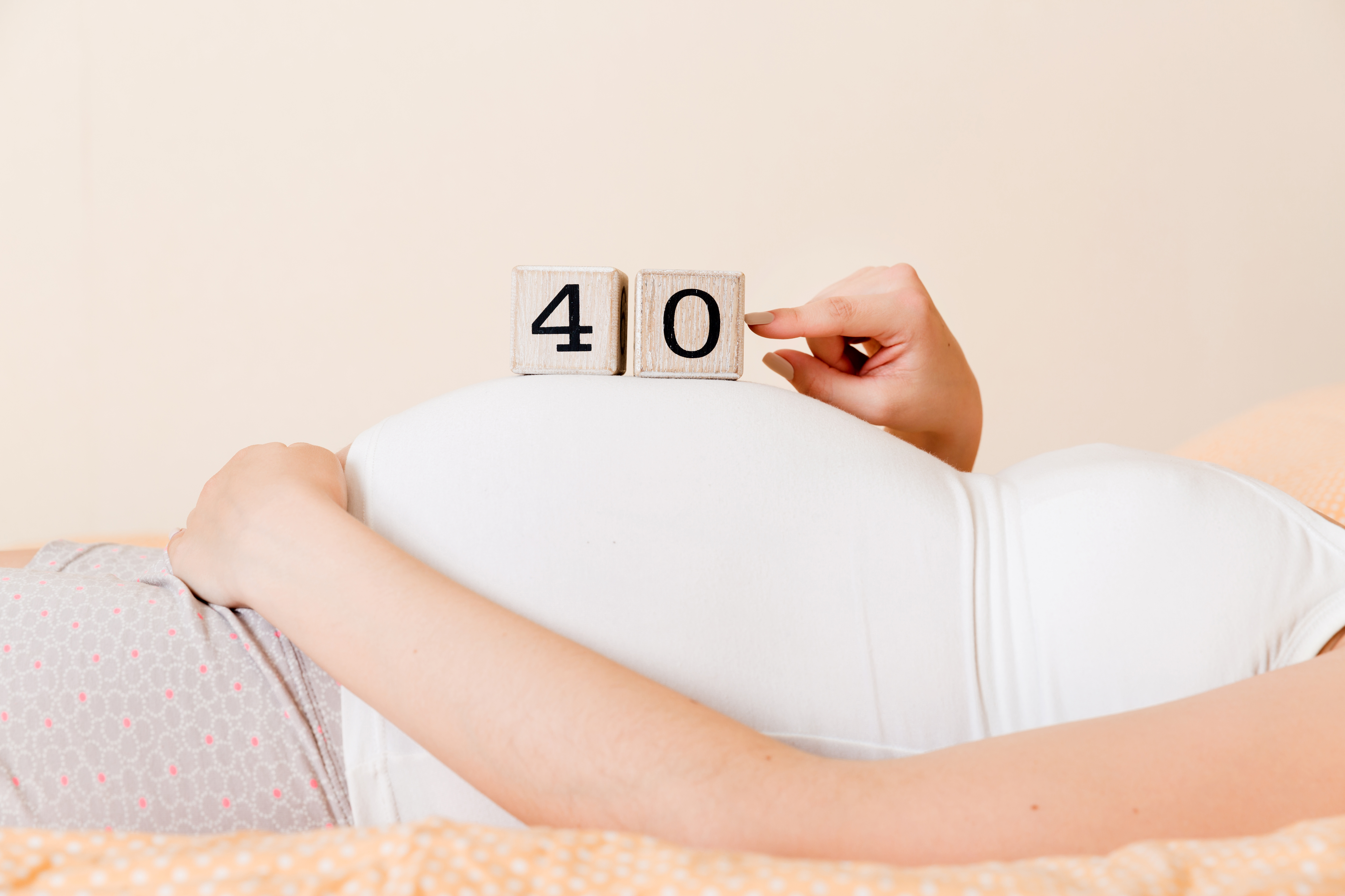 Pregnant woman in white underwear on bed in home holding calendar with weeks 40 of pregnant. Maternity concept. Expecting an upcoming baby