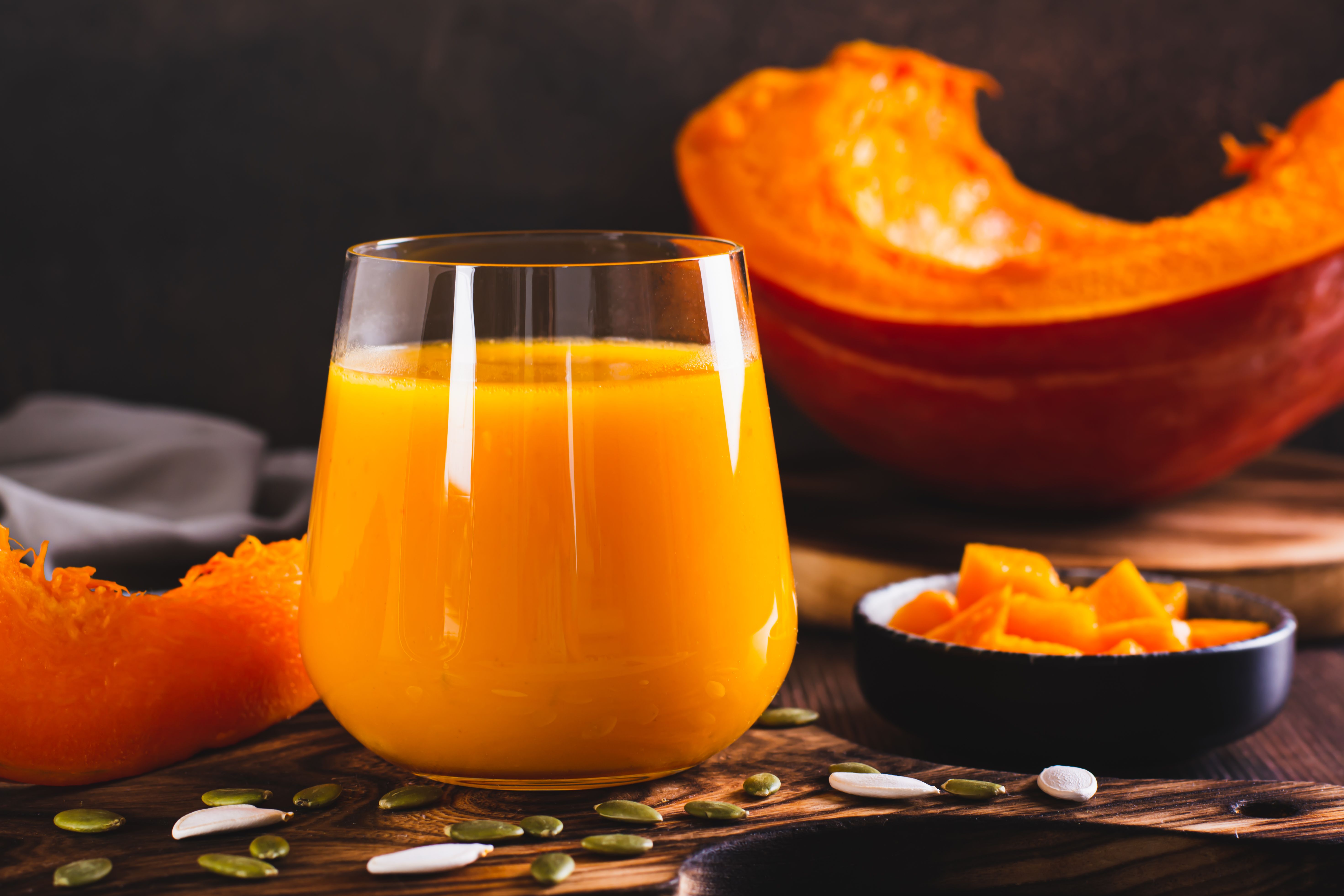 Fresh pumpkin juice in a glass, seeds and pieces of pumpkin on the table