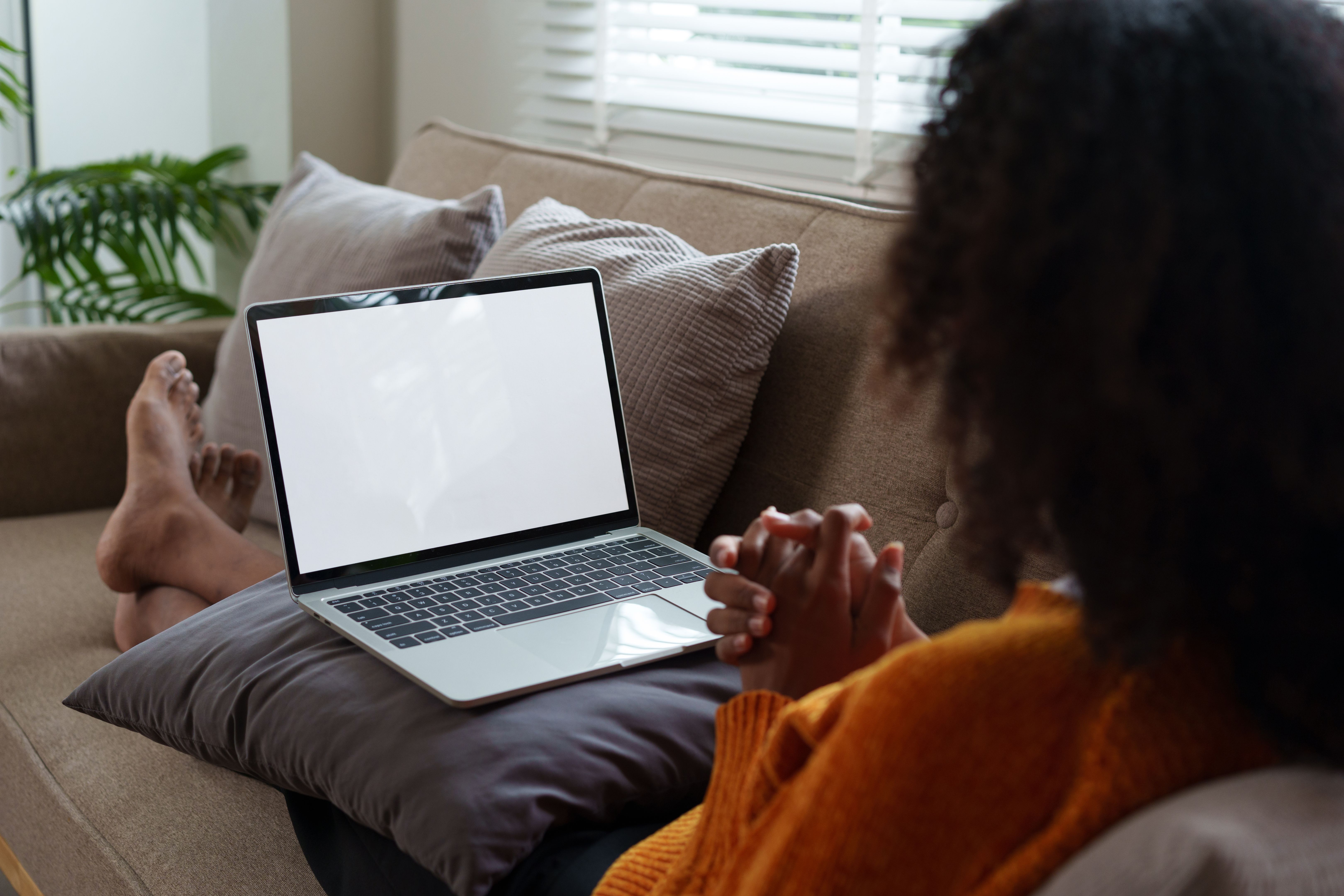Afro American woman relaxing on couch, using laptop with blank screen at home. Afro American woman relaxing on couch, using laptop with blank screen at home.